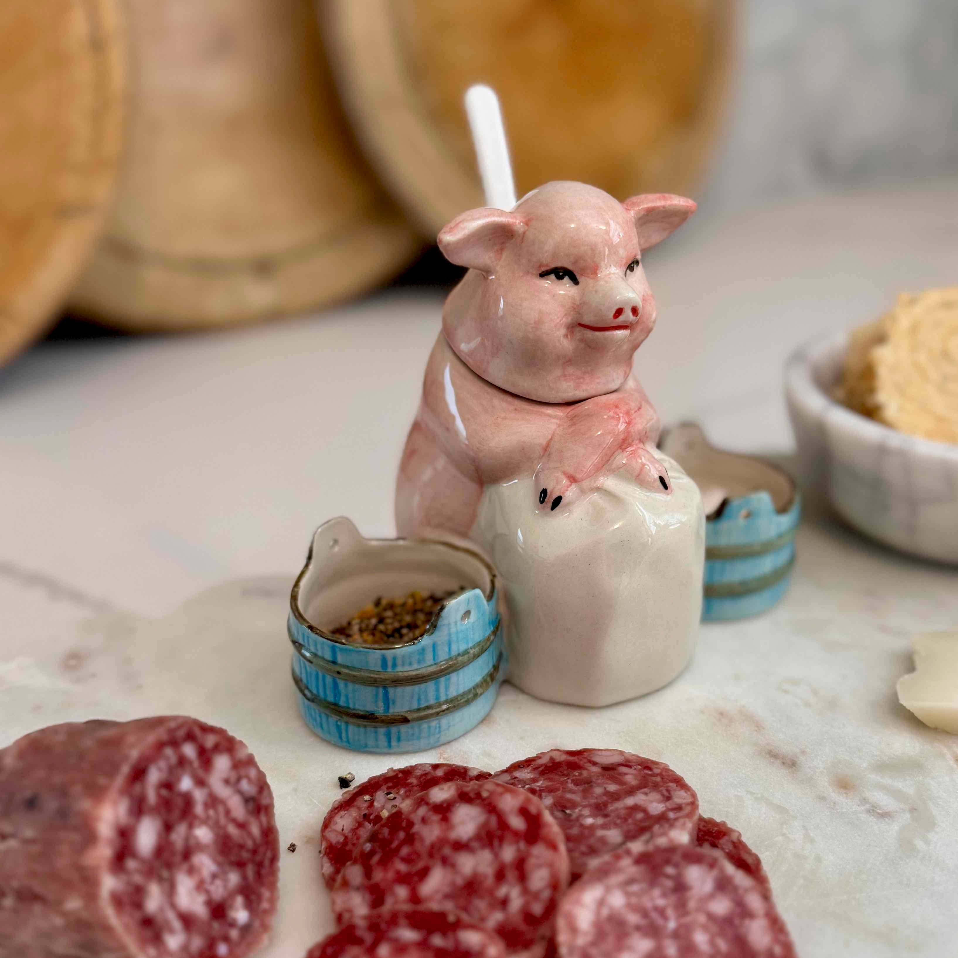 Pig-shaped salt shaker with pepper shaker on a marble surface with cured meats.