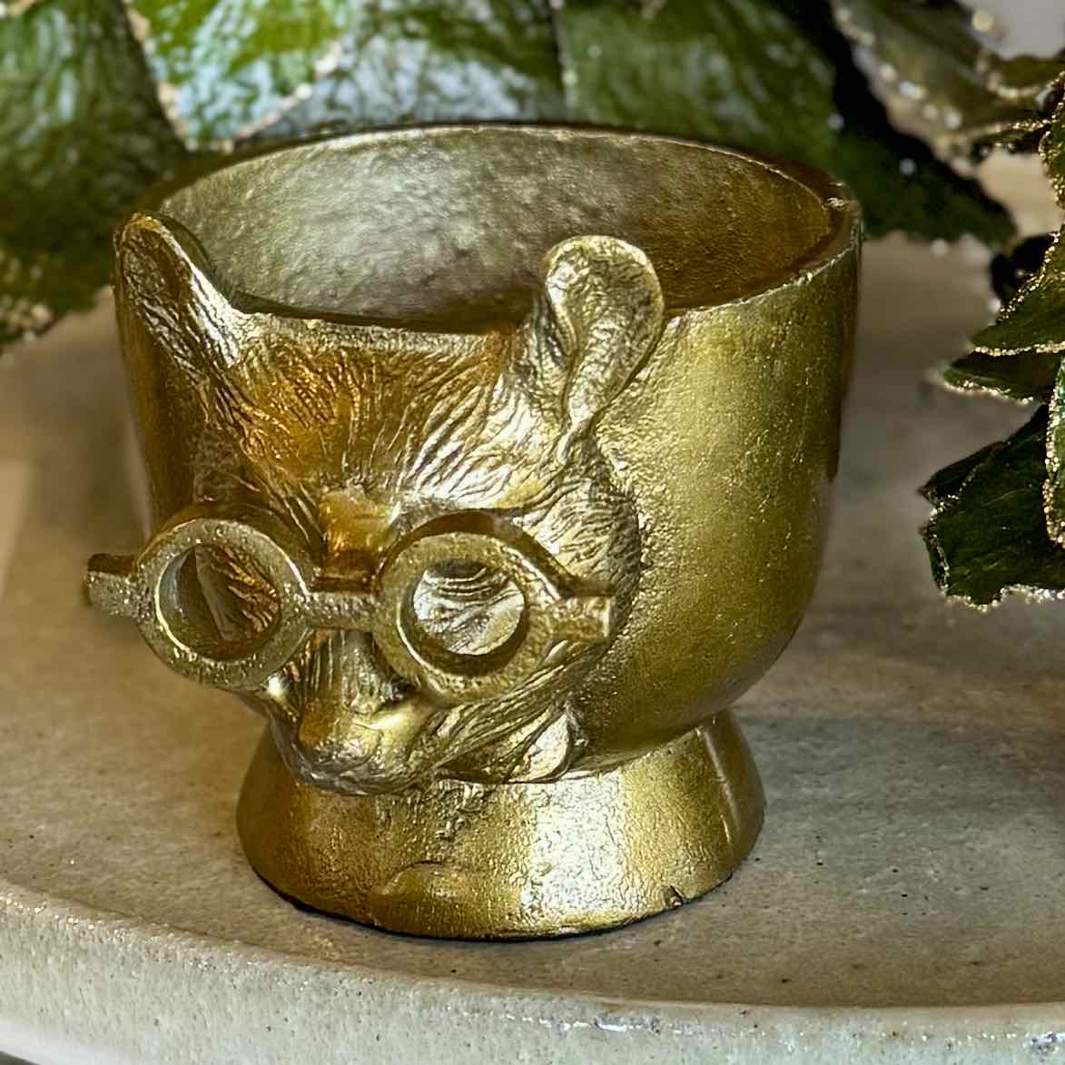 Gold cat-shaped object with glasses on a neutral background