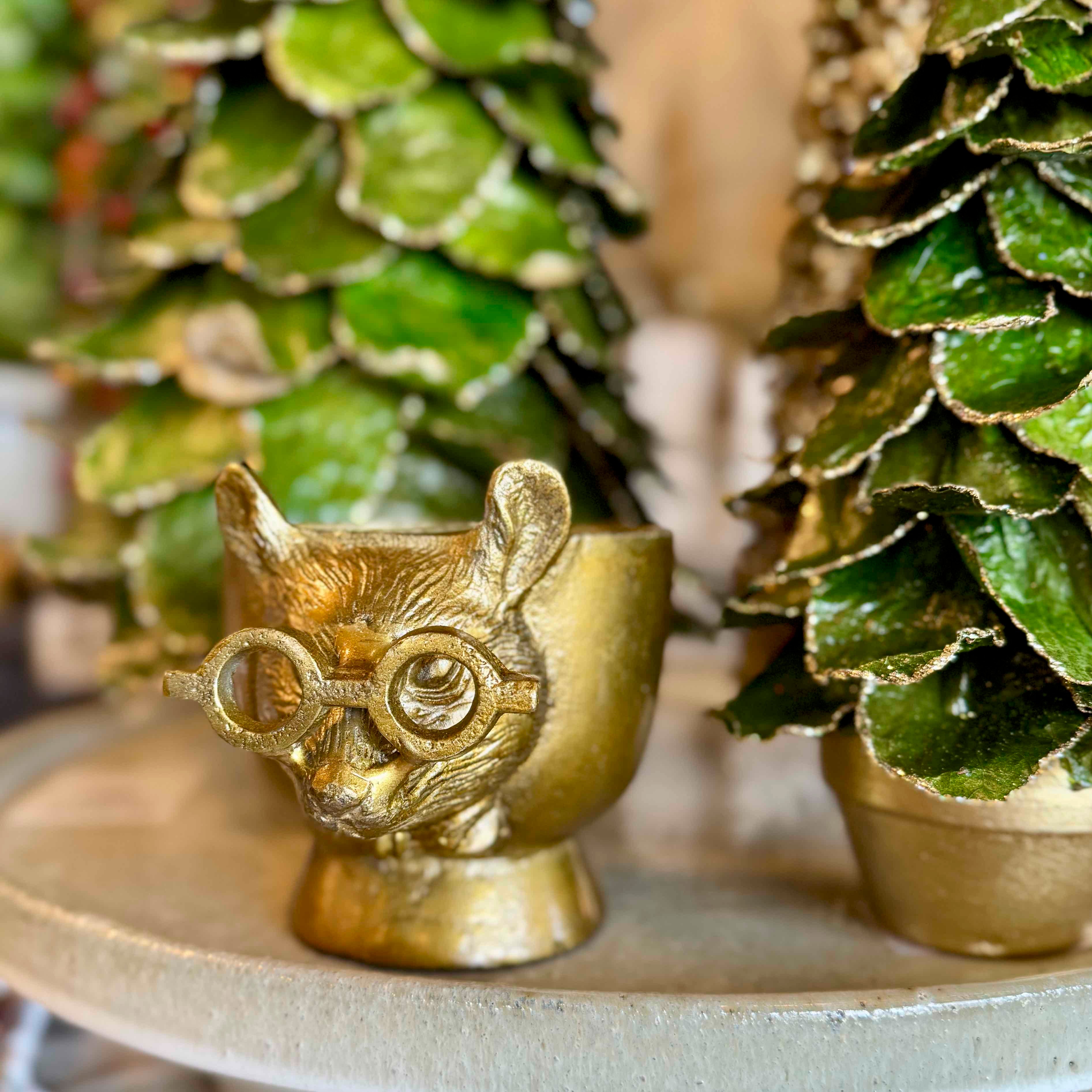 Gold owl-shaped container with decorative greenery in the background