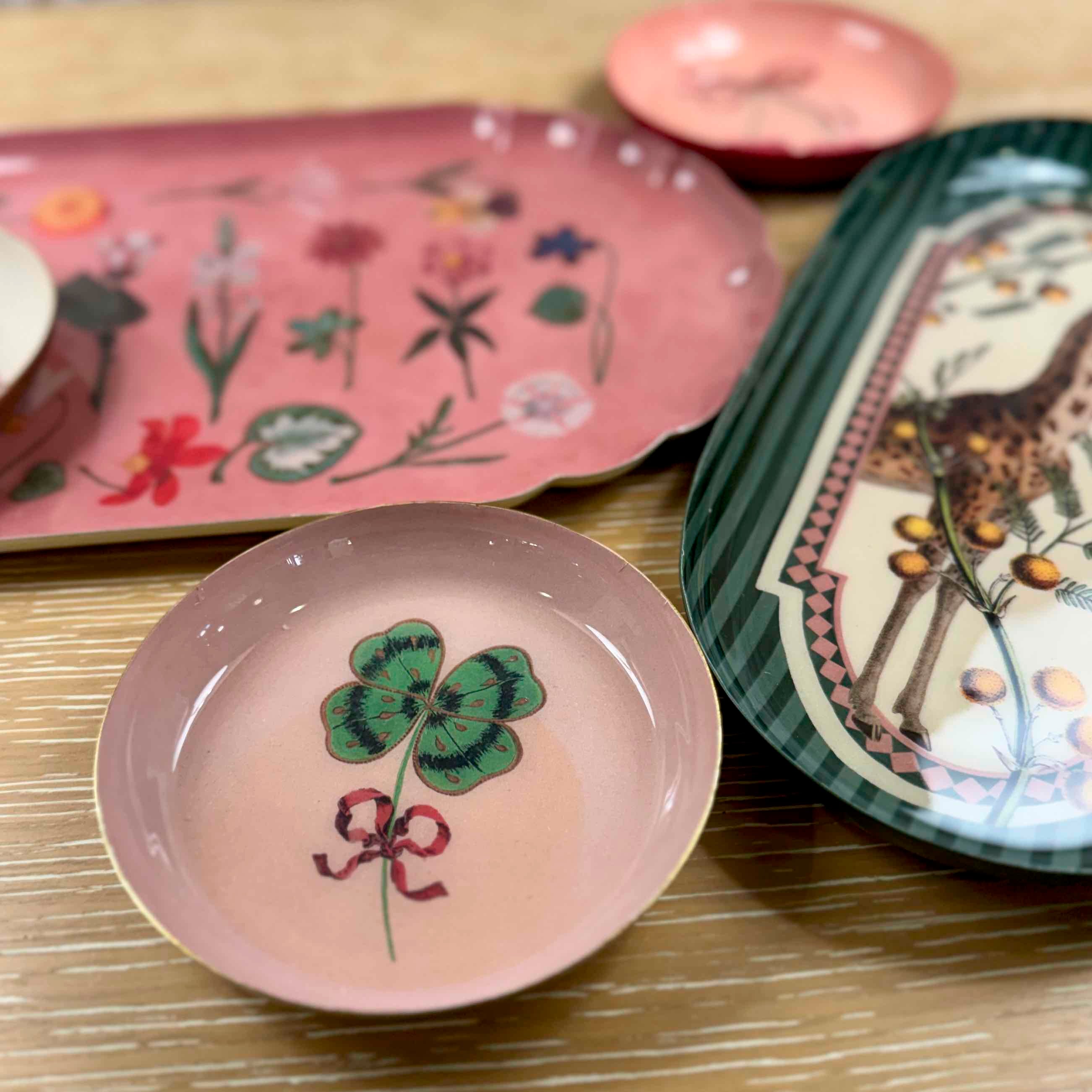 Collection of decorative plates with floral, animal, and clover designs on a wooden surface.