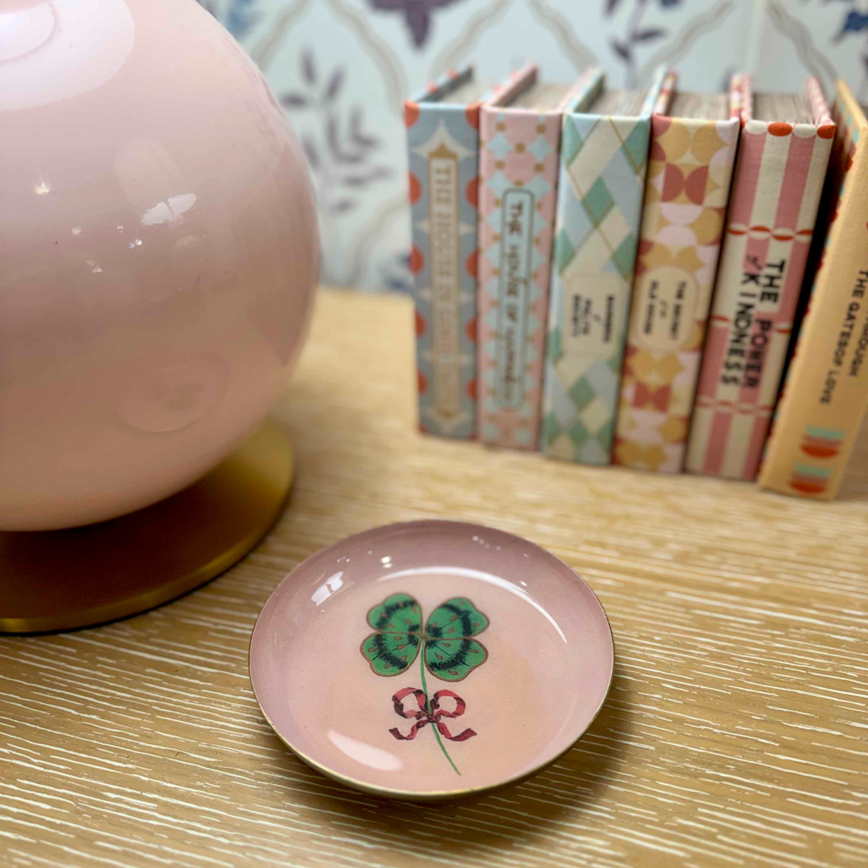 Small decorative plate with a clover design on a wooden surface, with books in the background.