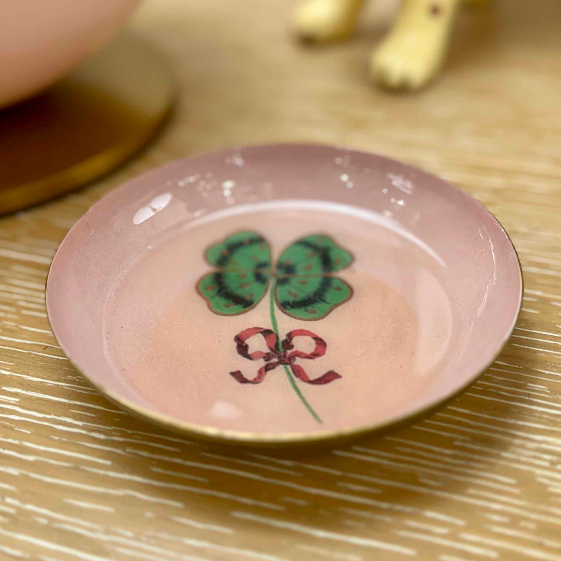 Small pink ceramic dish with floral design on a gold surface