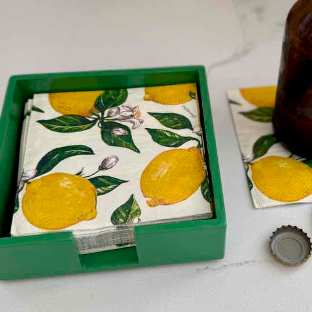 Set of lemon-patterned napkins in a green box on a white surface.