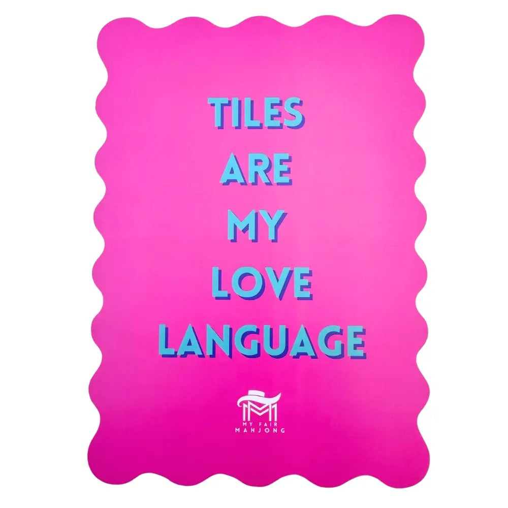 A bright pink rectangular mat with wavy scalloped edges, featuring the text 'TILES ARE MY LOVE LANGUAGE' in light blue 3D-style letters. A small white logo for 'MASTONE' is visible at the bottom center.