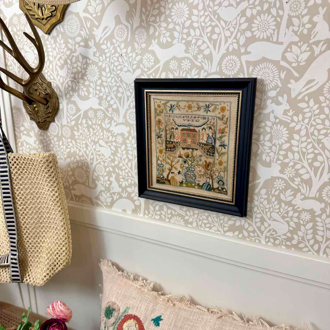 Framed embroidered artwork on a wall with decorative wallpaper and decor items.