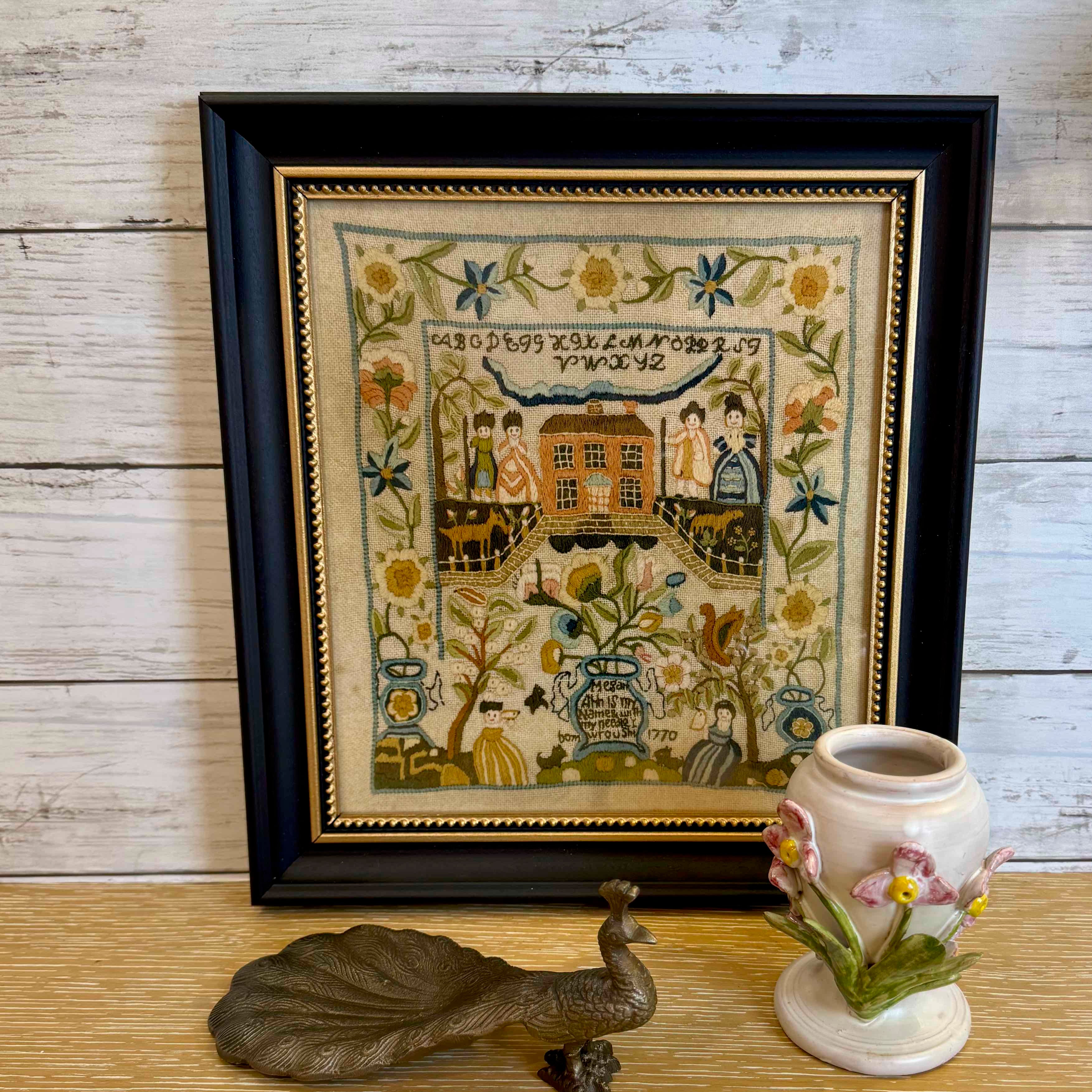 Framed needlepoint with decorative elements on a wooden surface