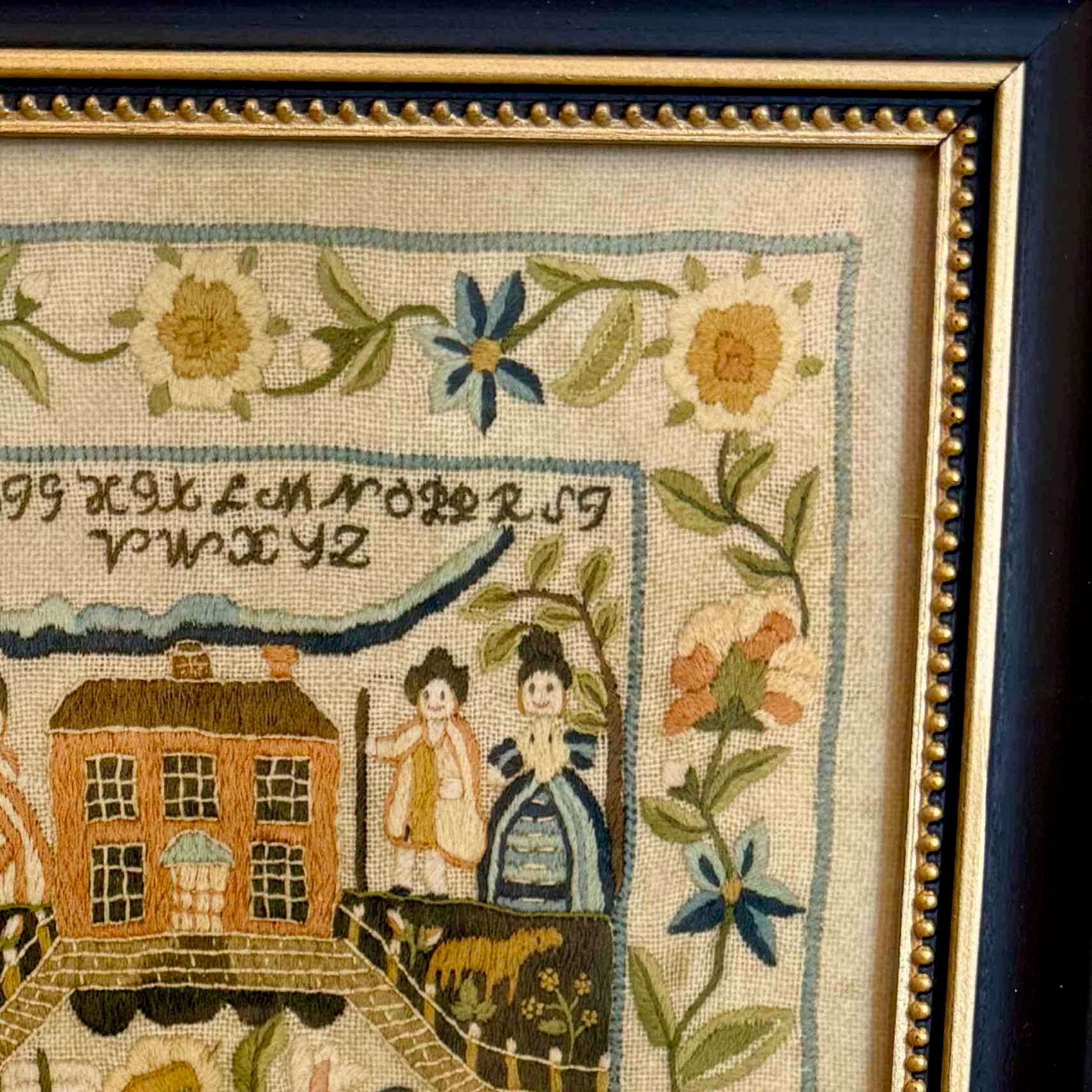 Framed needlepoint with house, people, and floral elements