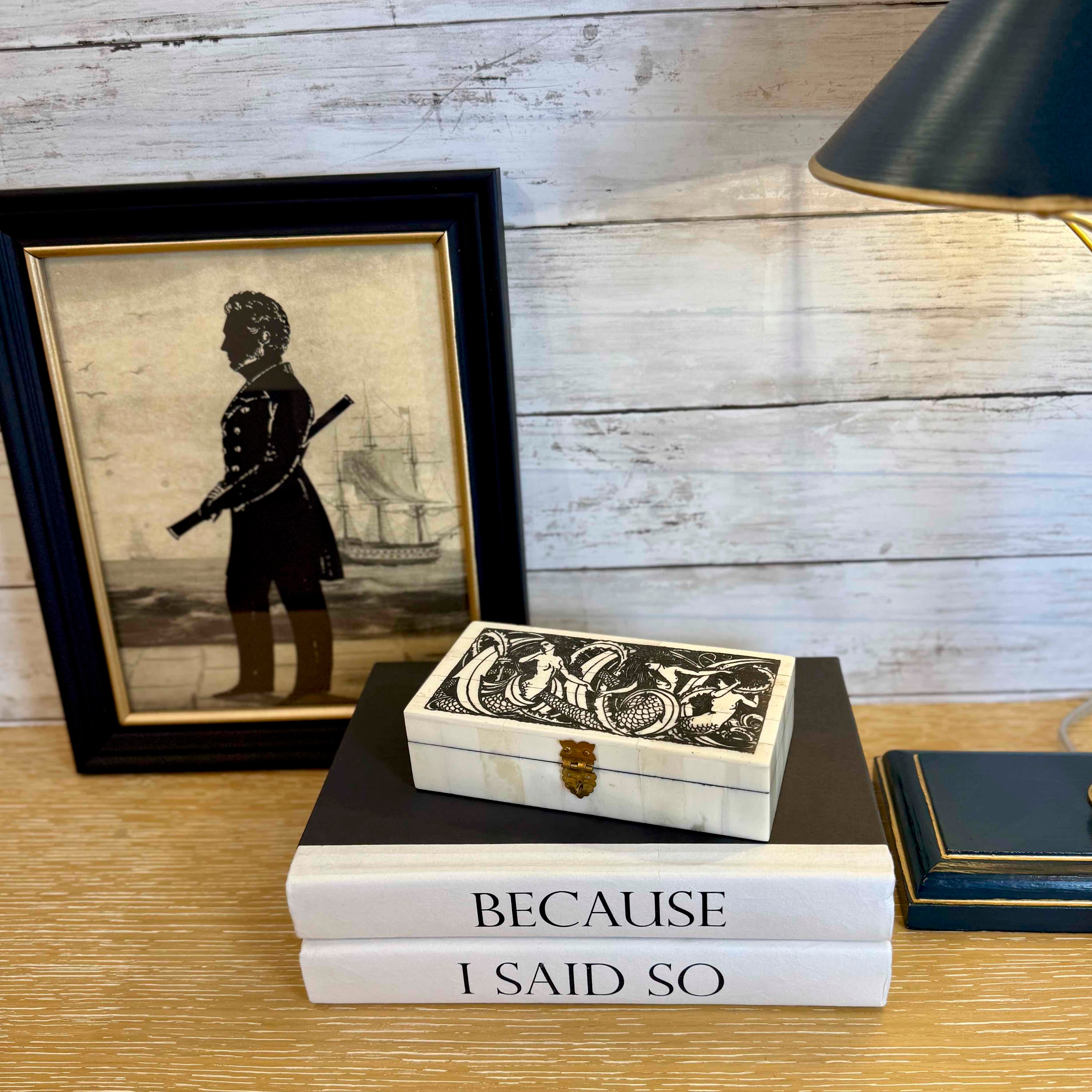 Stack of books with a decorative box and framed silhouette on a wooden surface.