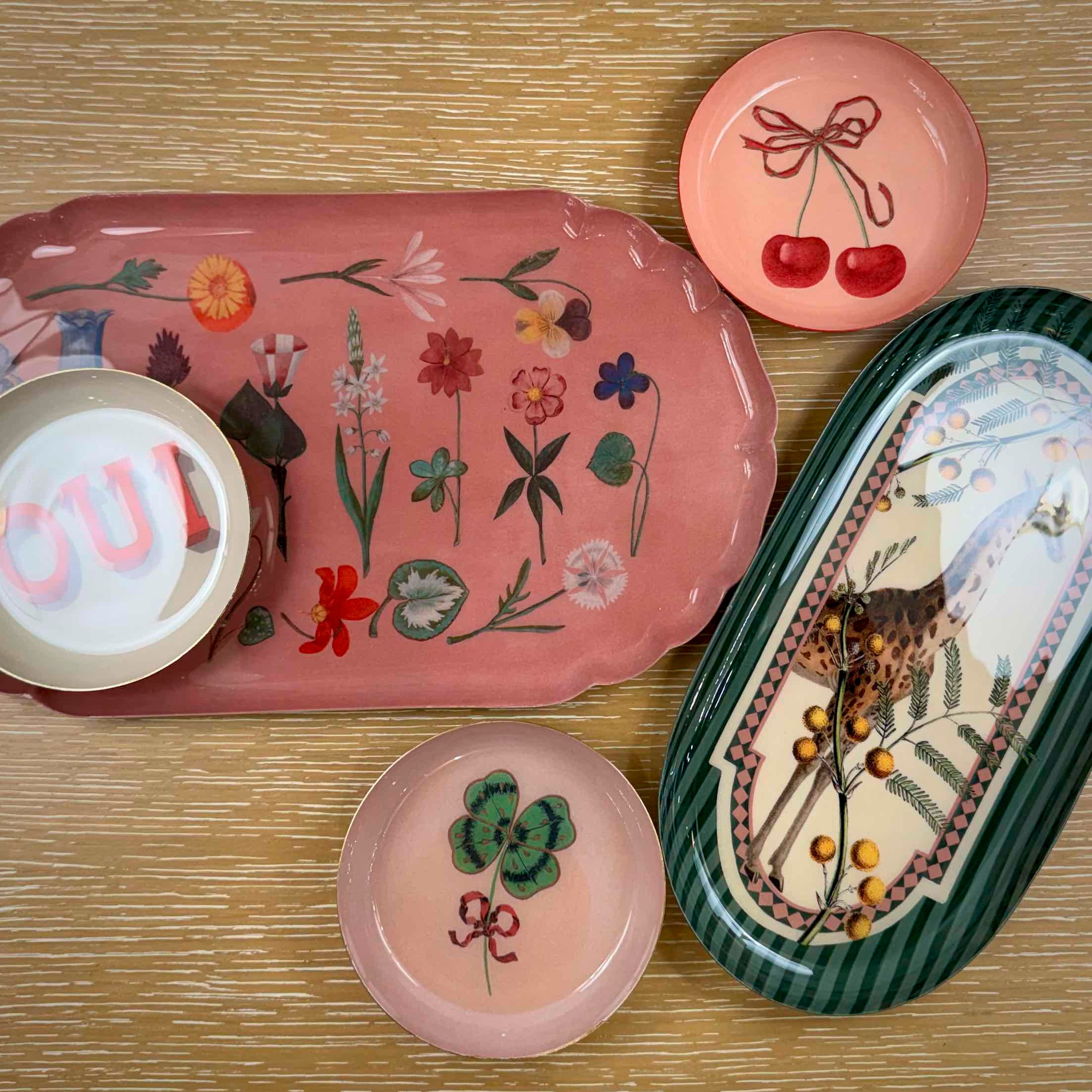 Collection of decorative ceramic items including a pink floral tray, small pink plate with cherries, and a green and white oval dish with a design.