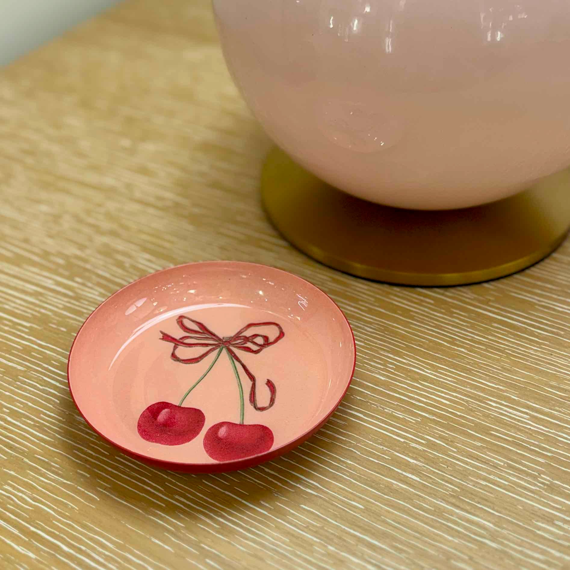 Small pink ceramic dish with cherry design on a textured surface