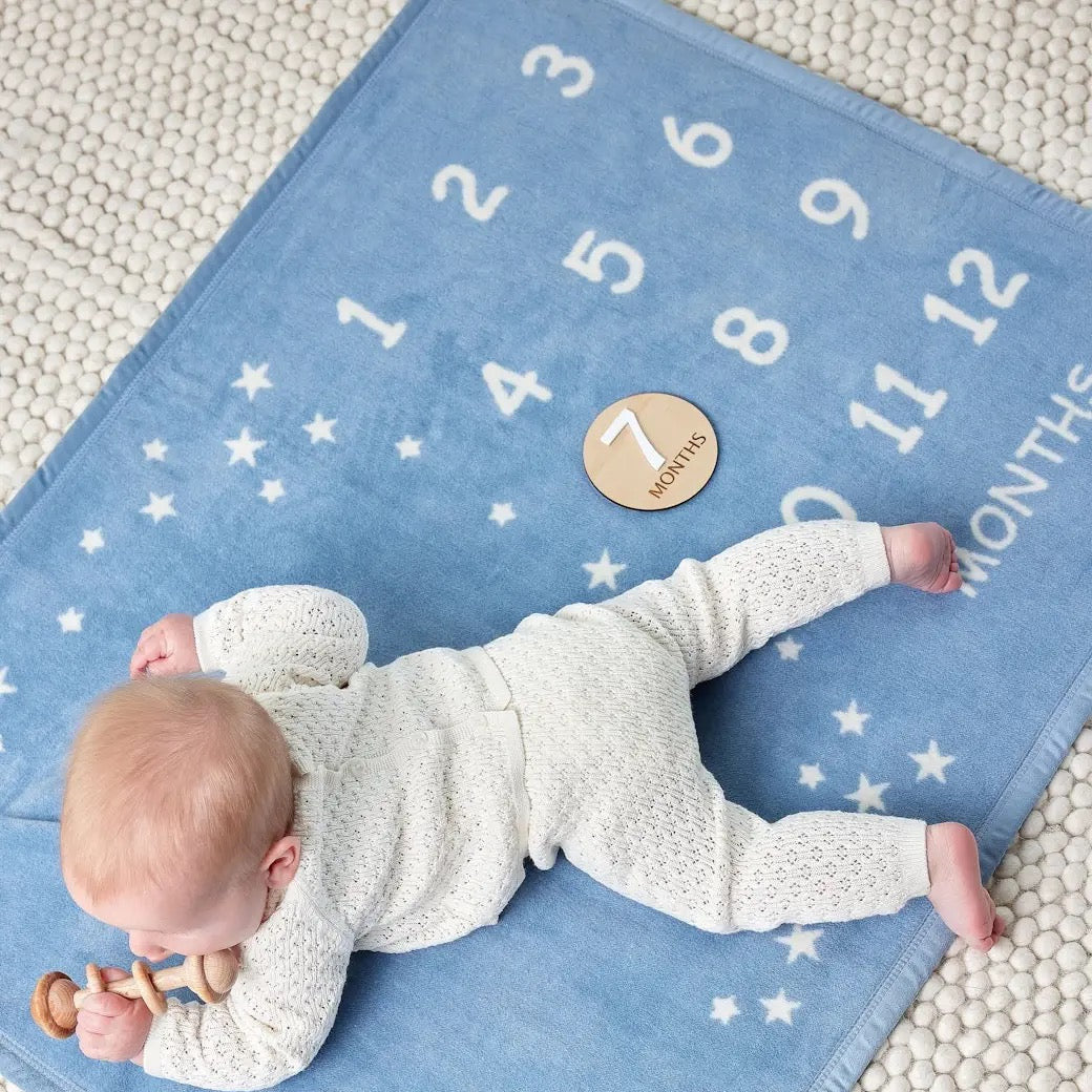 Baby lying on a blue mat with numbers and stars, indicating months of age.