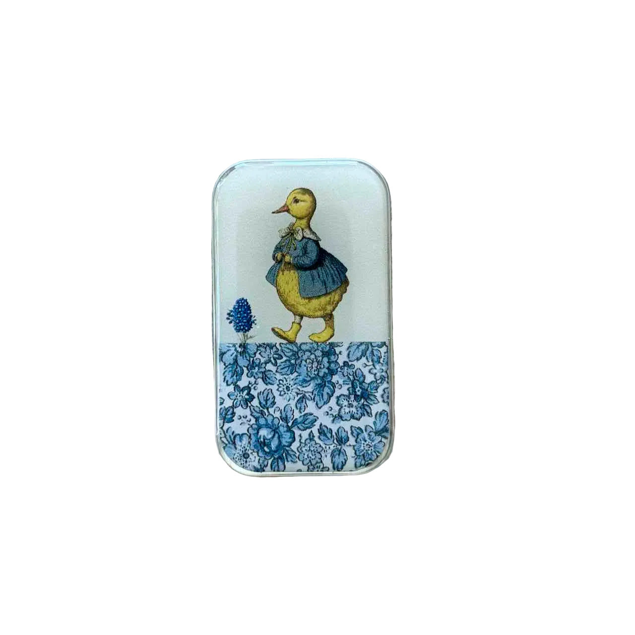 A small rectangular tin with rounded corners, featuring a vintage-style illustration of a yellow duck in a blue dress on a white background, with a blue floral pattern along the bottom. The tin is placed on a light-colored wooden surface.
