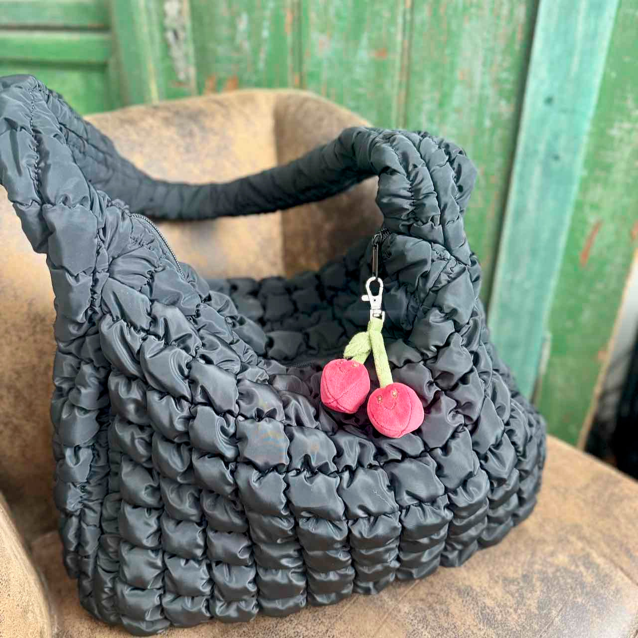 Black textured handbag with a cherry charm on a wooden surface