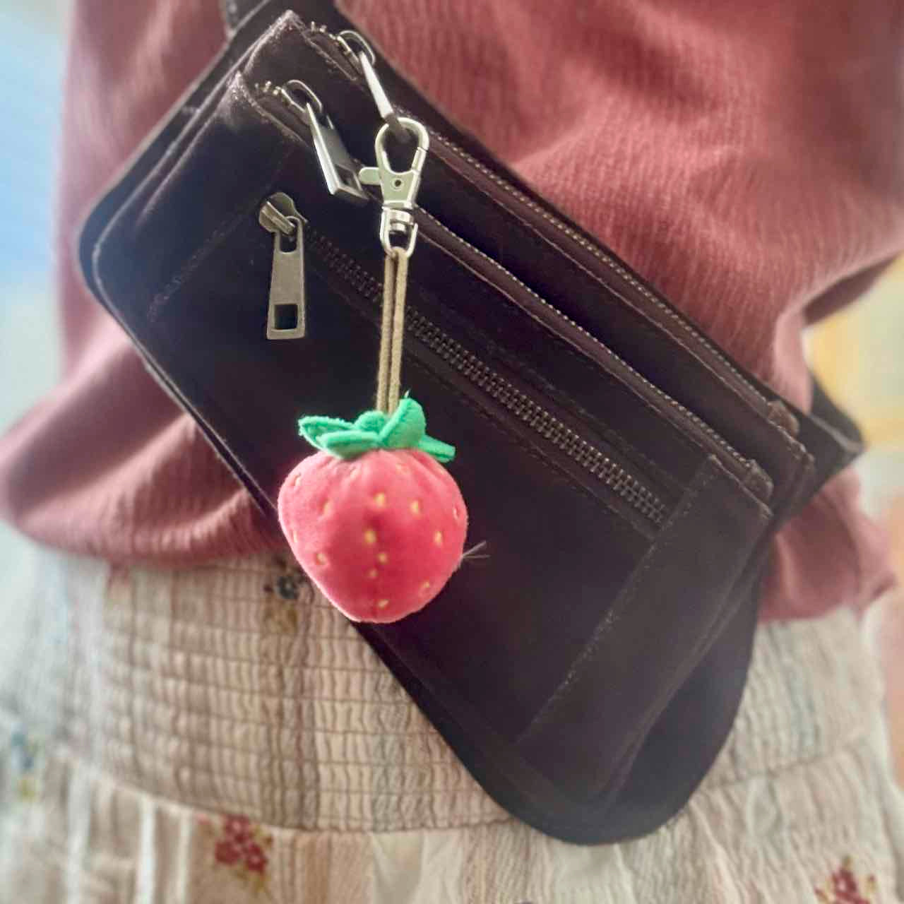 Black wallet with a strawberry-shaped keychain on a pink sweater background