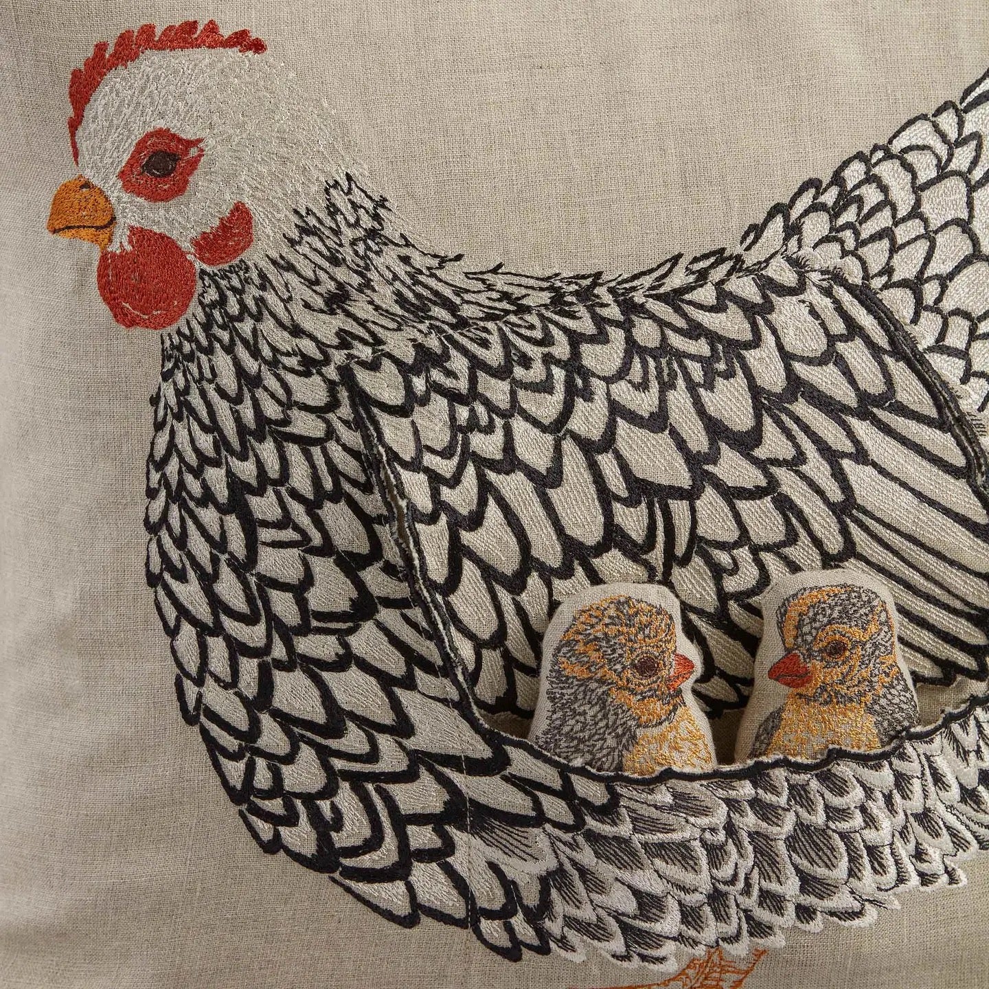 Embroidered hen and chicks design on a beige linen fabric, featuring a black and white feathered hen with red comb and wattle, with two small yellow and gray chicks nestled in the tail feathers.