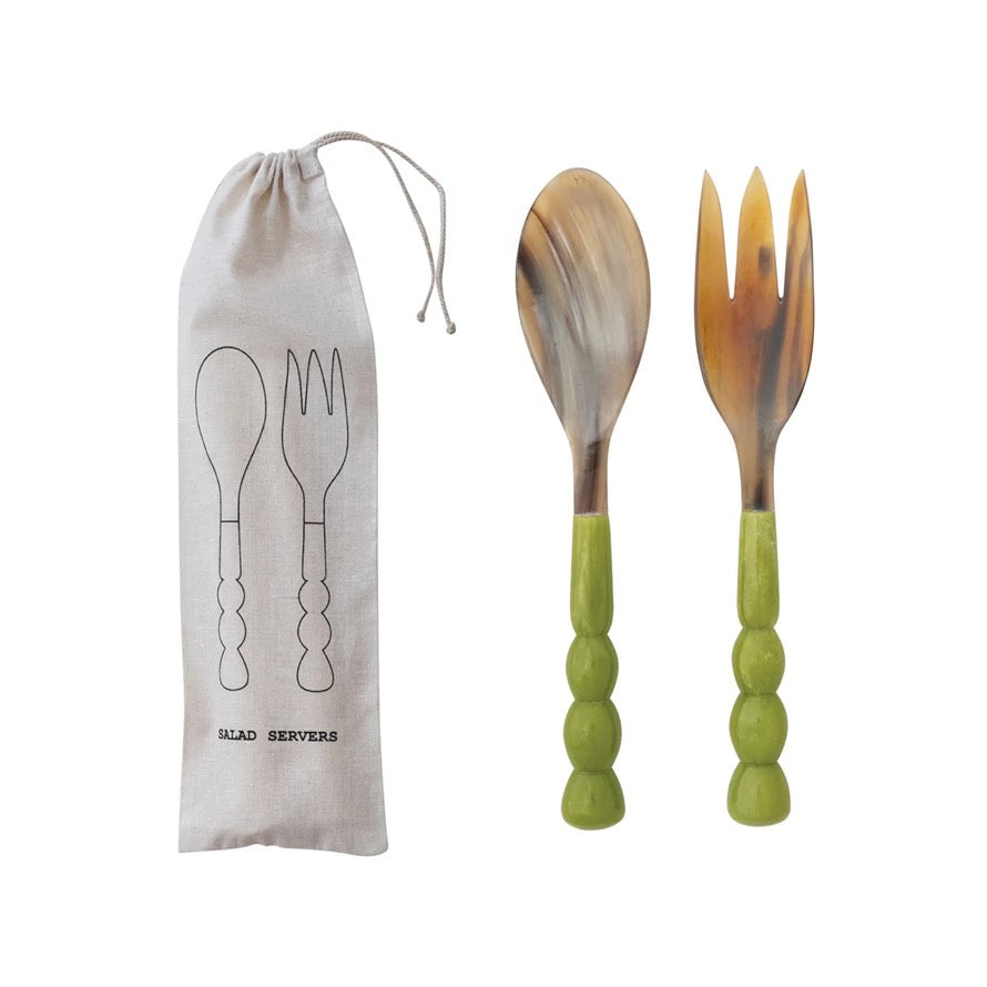 Set of salad servers with green handles and a carrying bag on a white background