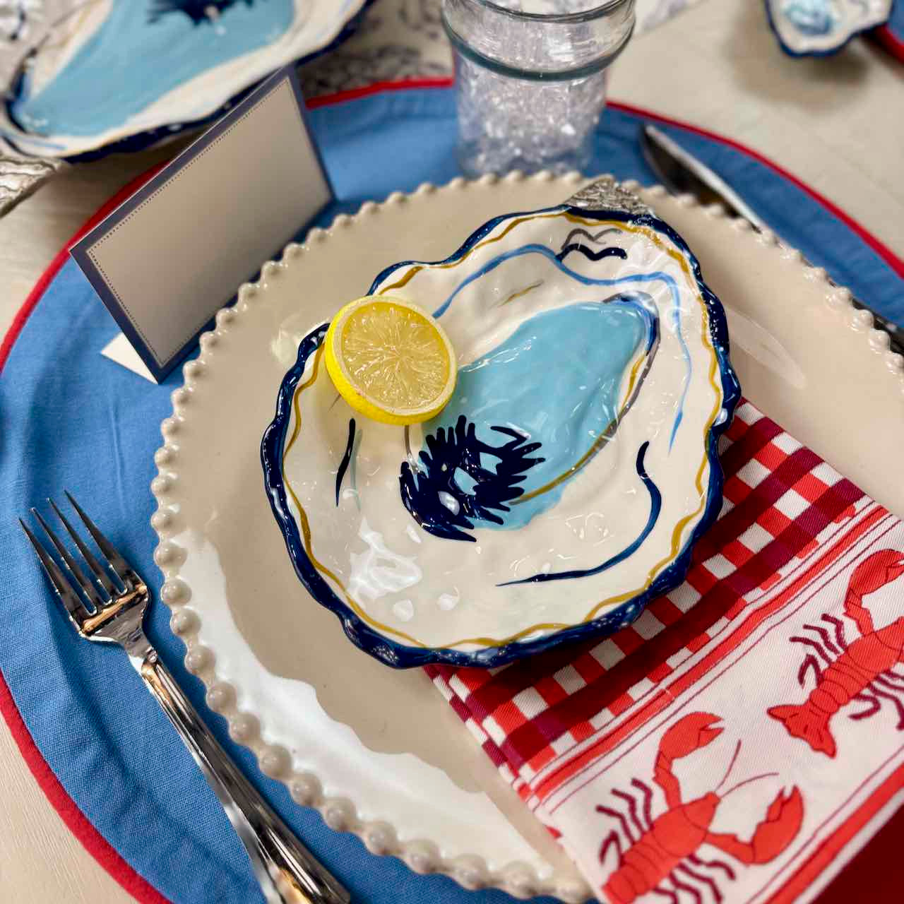 Decorative oyster shell with a lemon wedge on a table setting with a red and white checkered napkin.