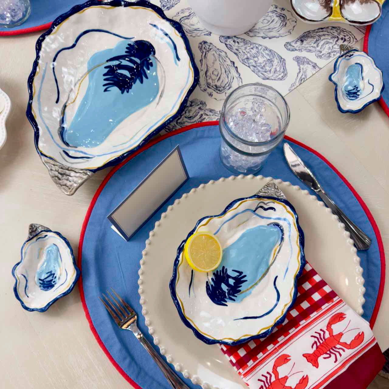 Table setting with oyster-themed plates and napkins on a blue and white tablecloth.