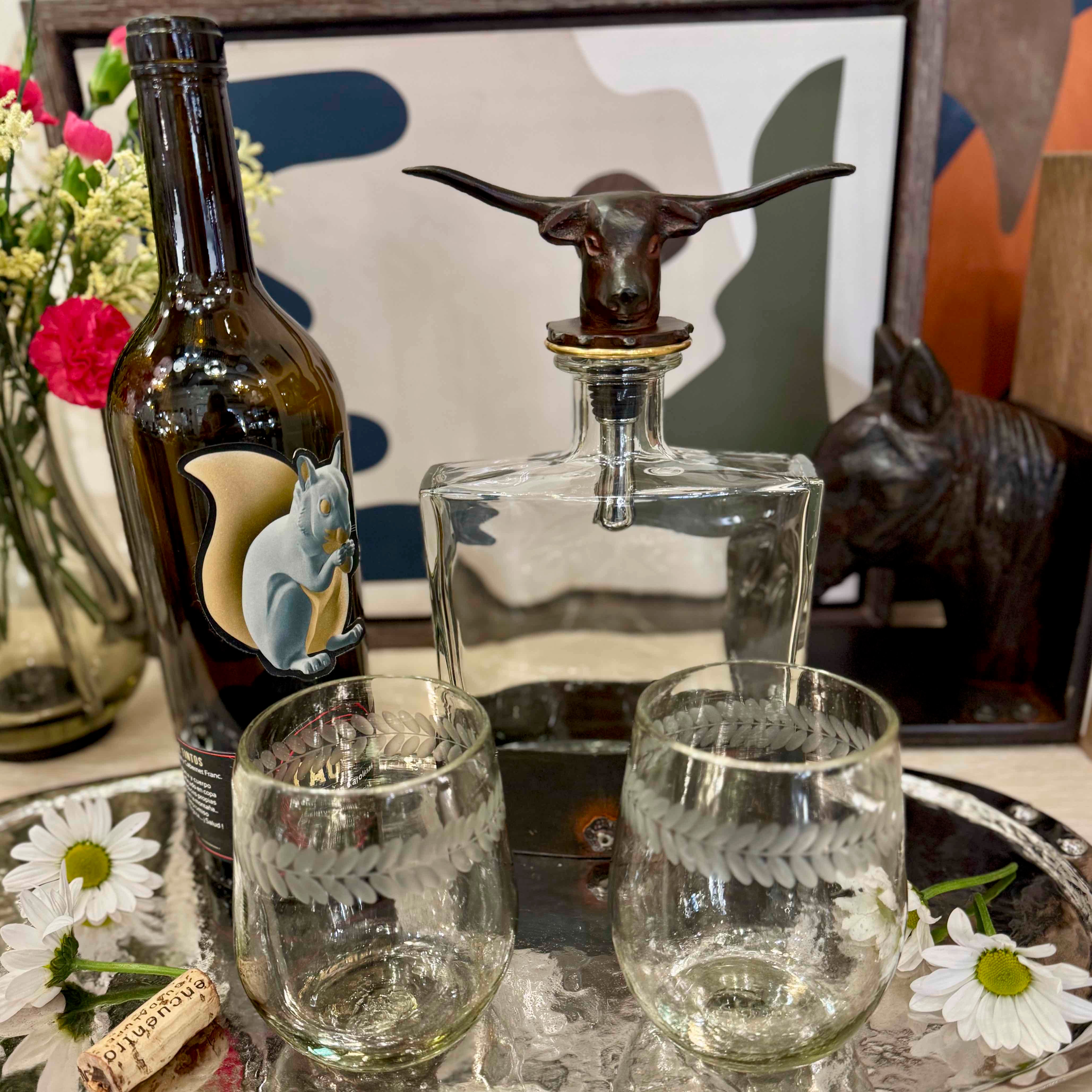 Wine bottle, decanter with bull stopper, and glasses on a table with decorative elements.