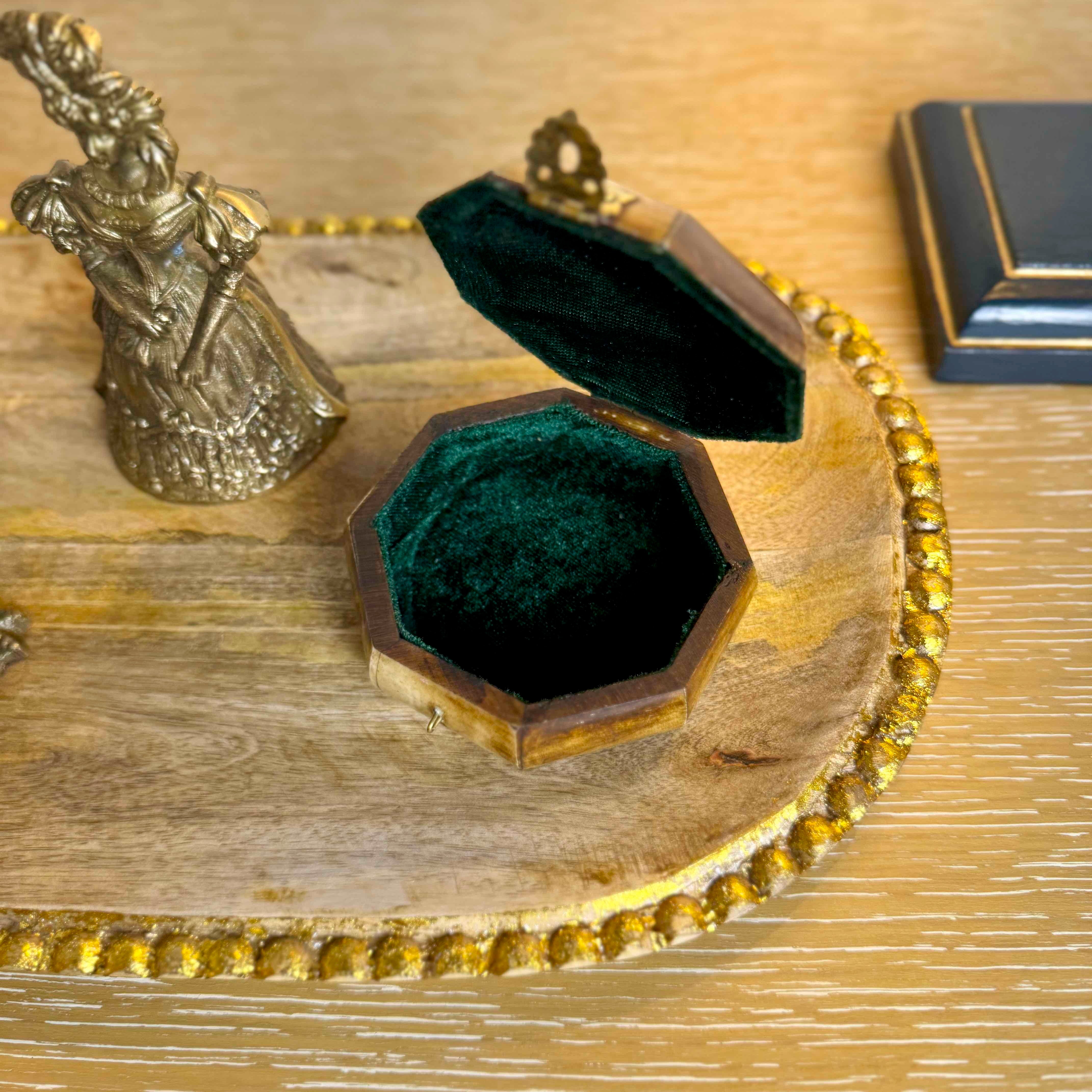 Hexagonal jewelry box with green interior on a wooden surface with decorative elements.