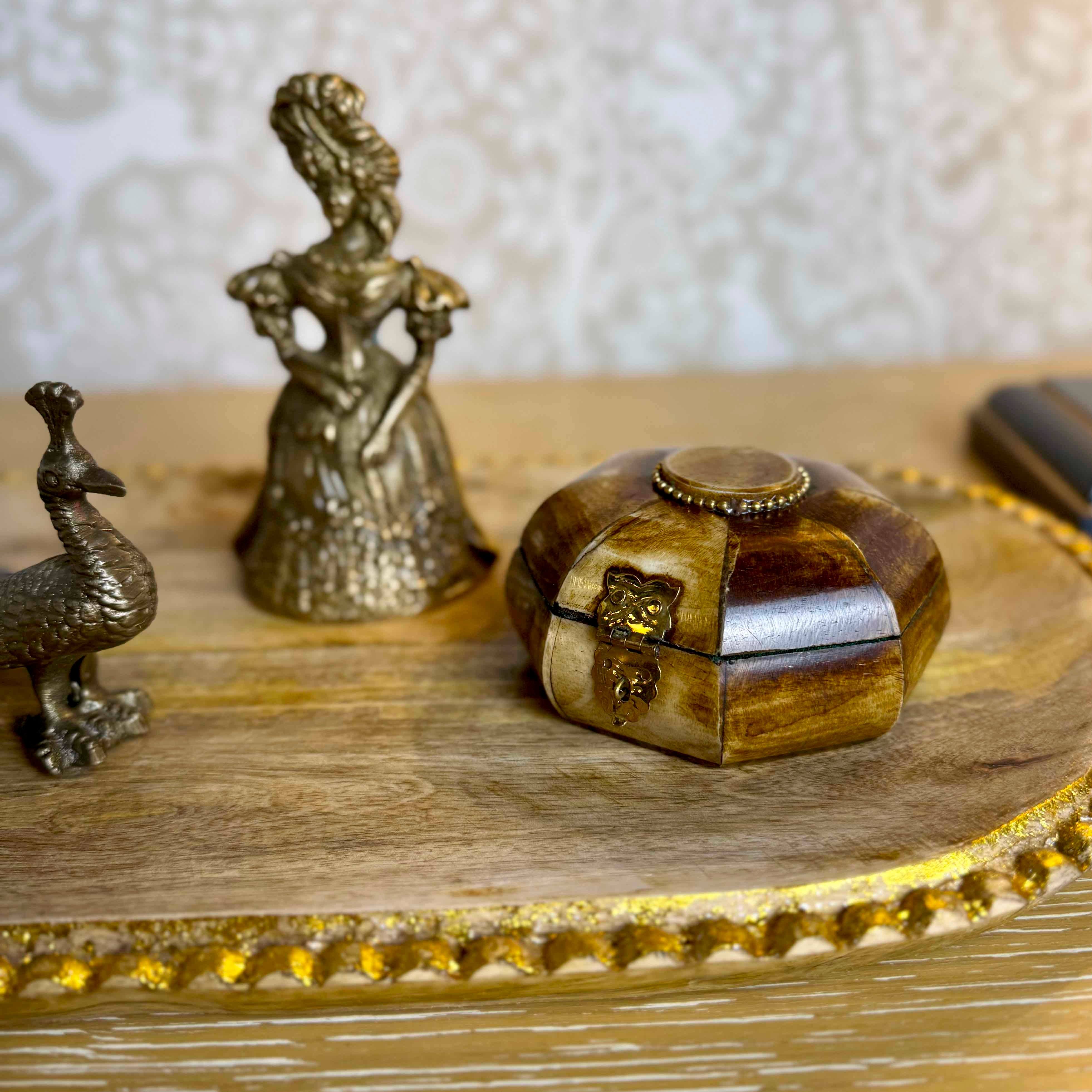 Decorative items including a small box, bird, and figure on a wooden surface with a textured background.