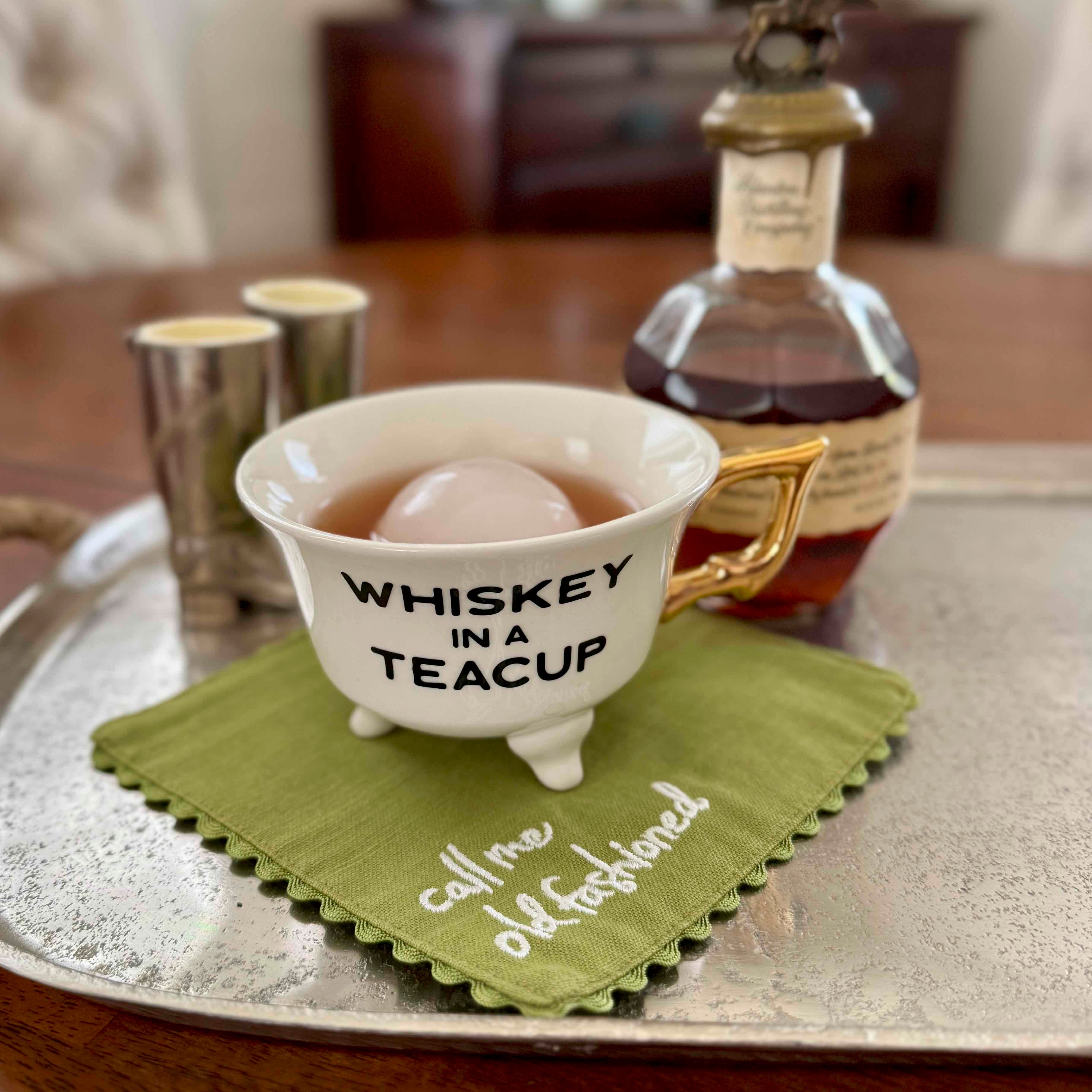 Teacup labeled 'Whiskey in a Teacup' with a bottle of whiskey on a tray.