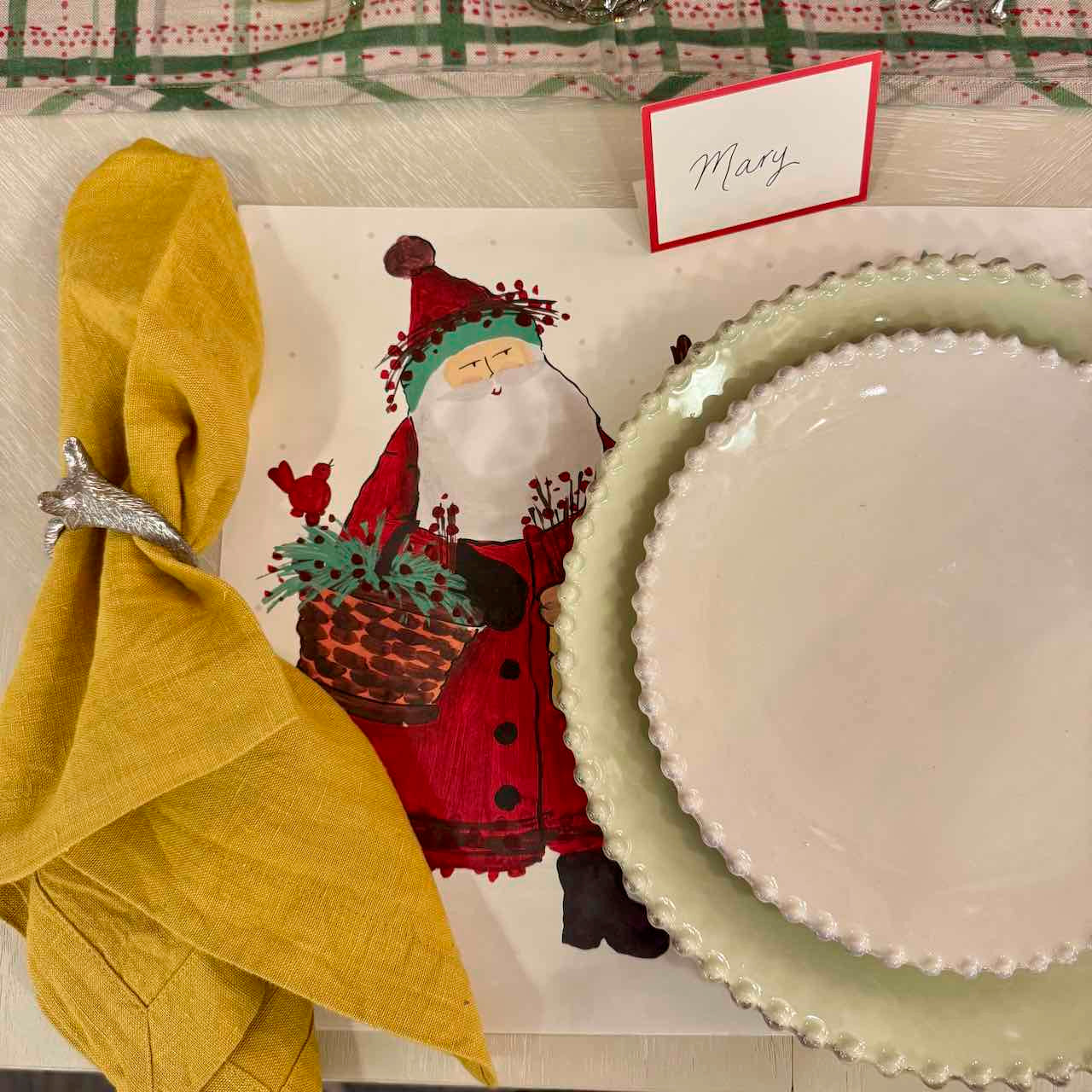 Christmas-themed table setting with Santa Claus card, yellow napkin, and green plate.