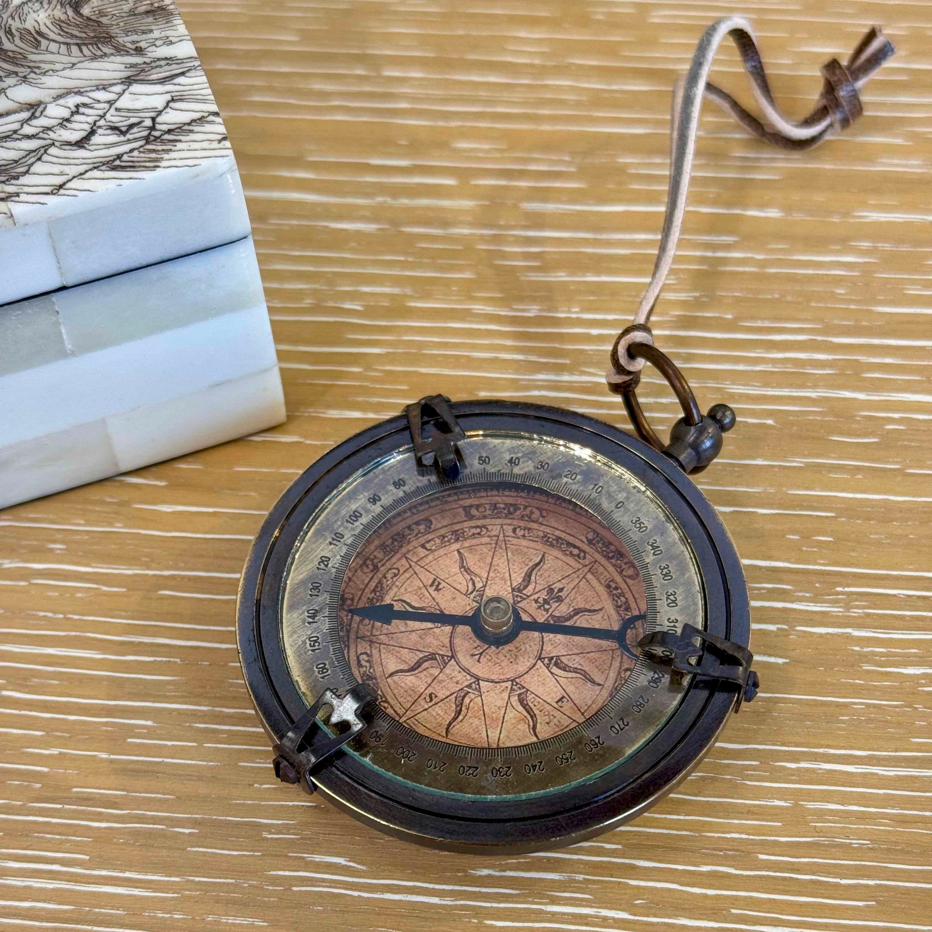 Vintage-style compass on a wooden surface with a book in the background