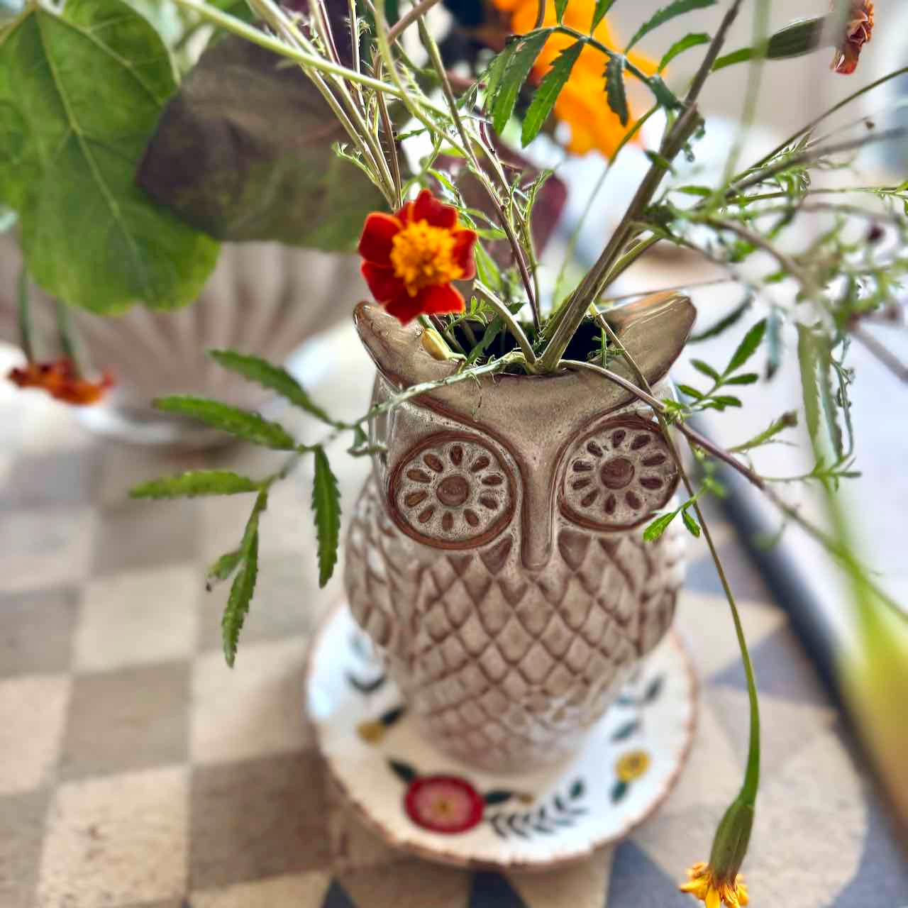 Owl-shaped ceramic planter with flowers on a checkered tablecloth