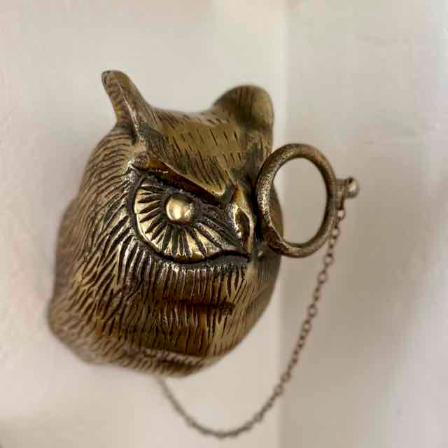 Bronze owl-shaped object with a chain on a white background