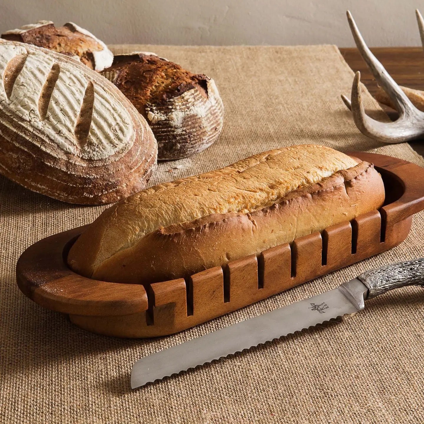 Loaves of bread on a wooden board with a bread knife on a textured surface