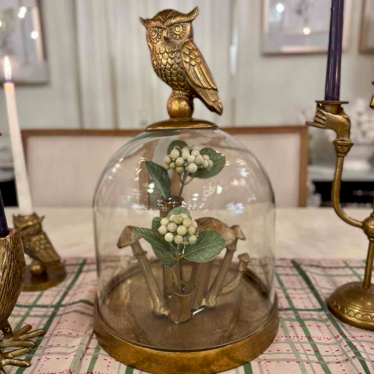 Decorative item with a glass dome, gold owl, and floral arrangement on a table.