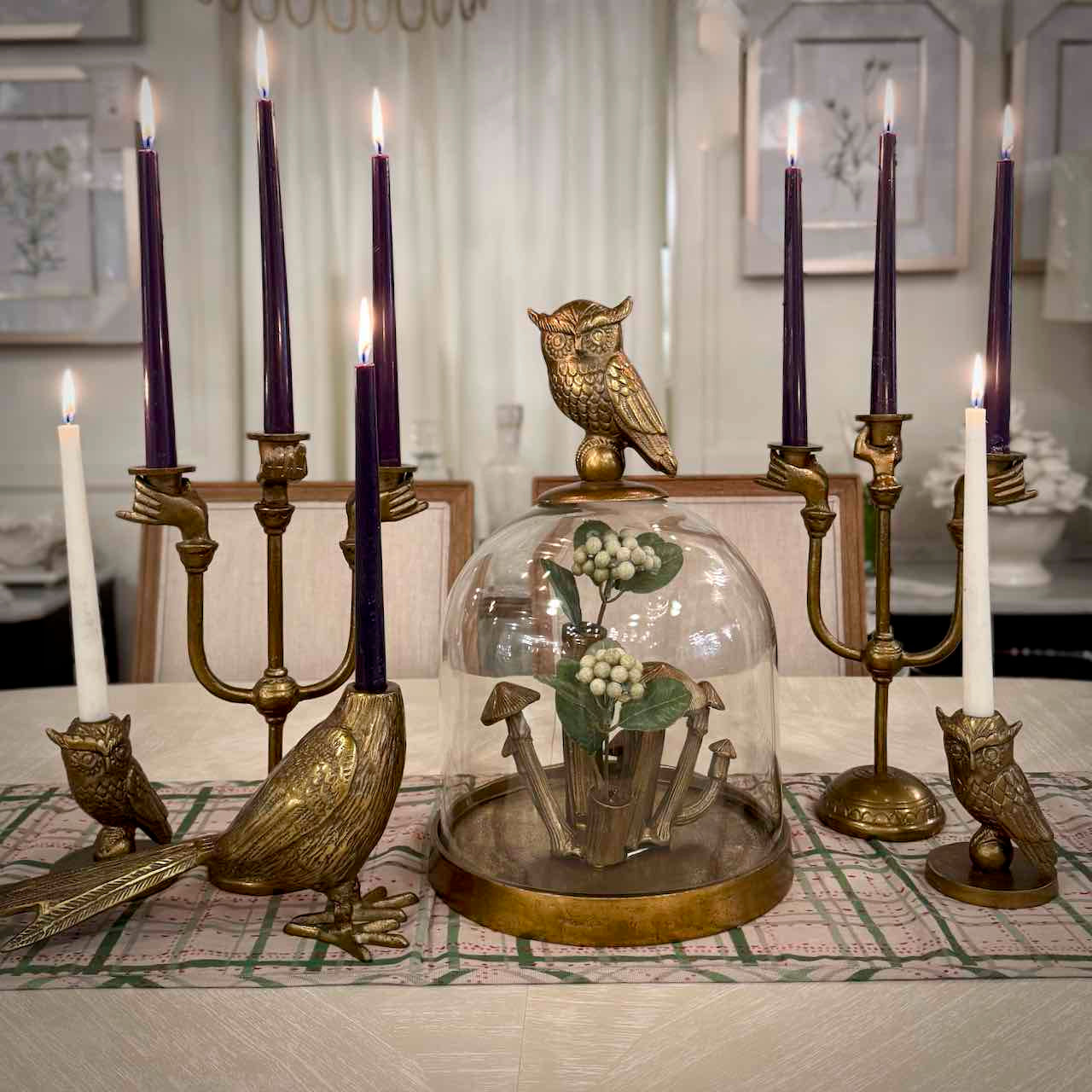 Decorative setup with brass candle holders, purple candles, and a glass dome with decorative elements on a table.