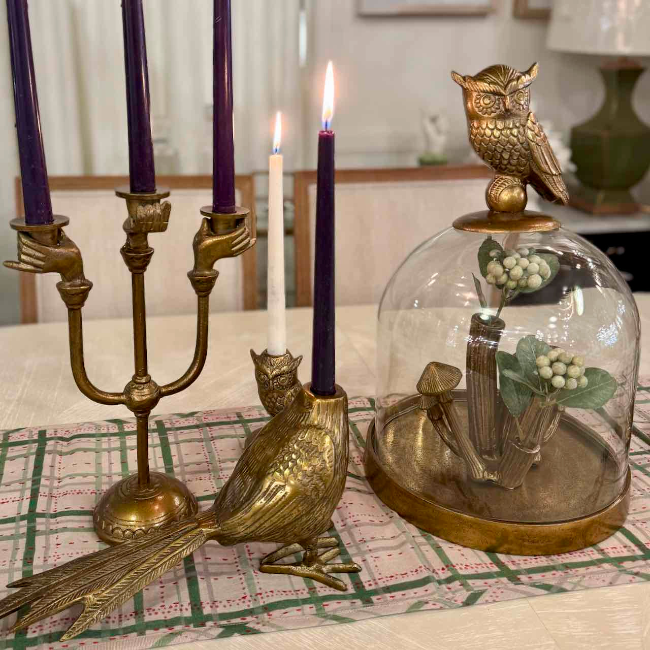 Decorative table setting with brass owl candle holder, glass dome, and candles on a checkered tablecloth.