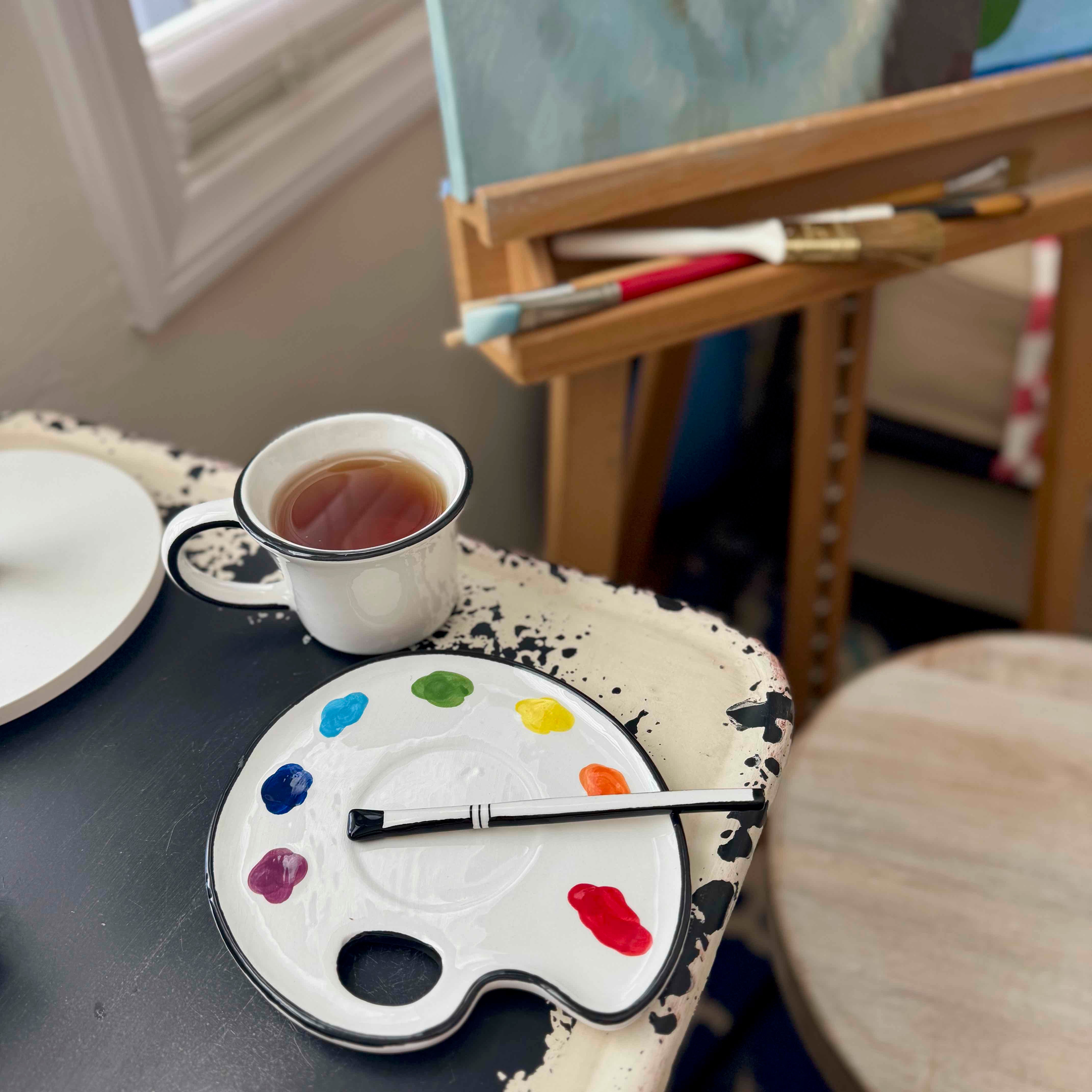 Artistic setup with a cup of tea, paintbrushes, and color palette on a table.