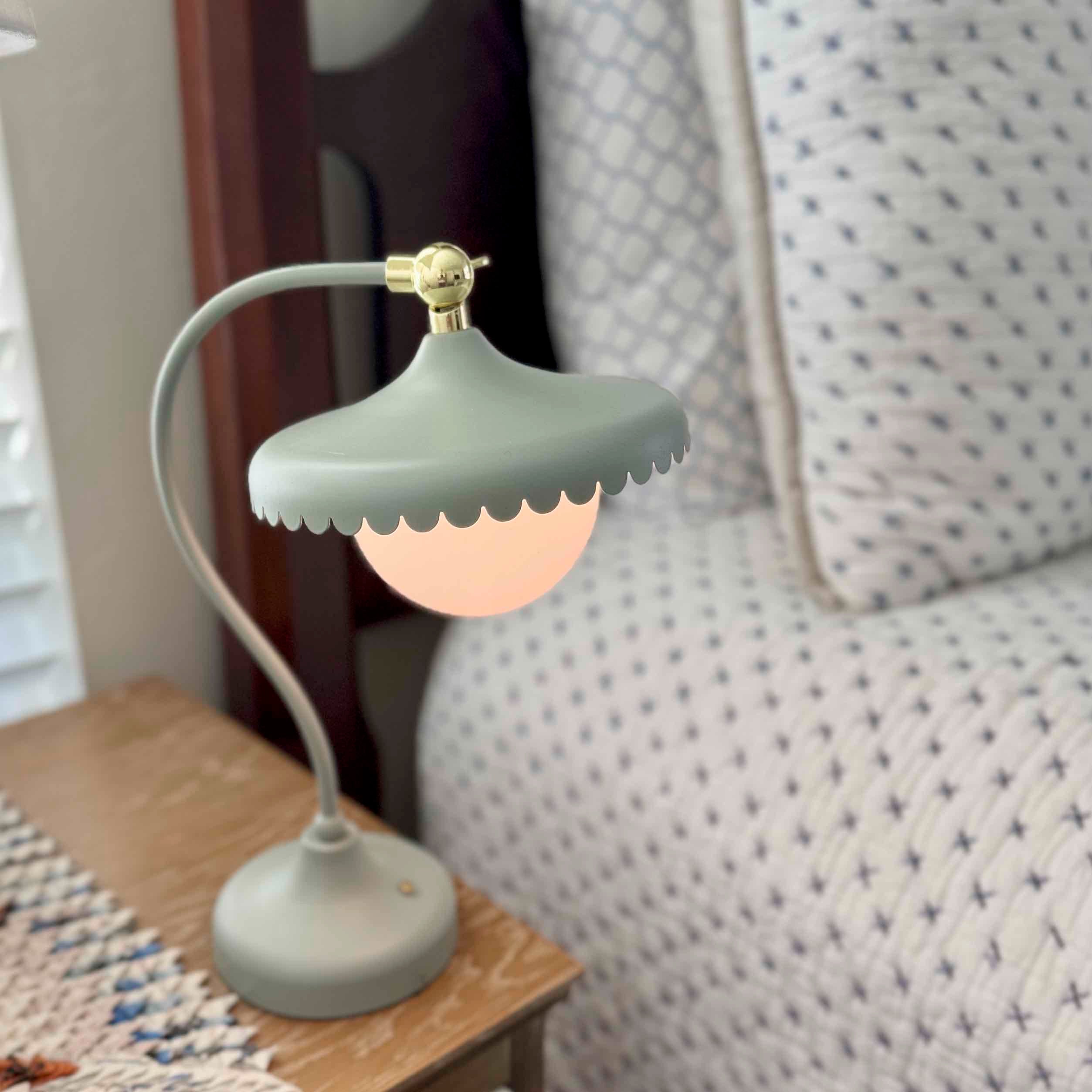 Small lamp with a green shade on a wooden surface next to a patterned fabric.