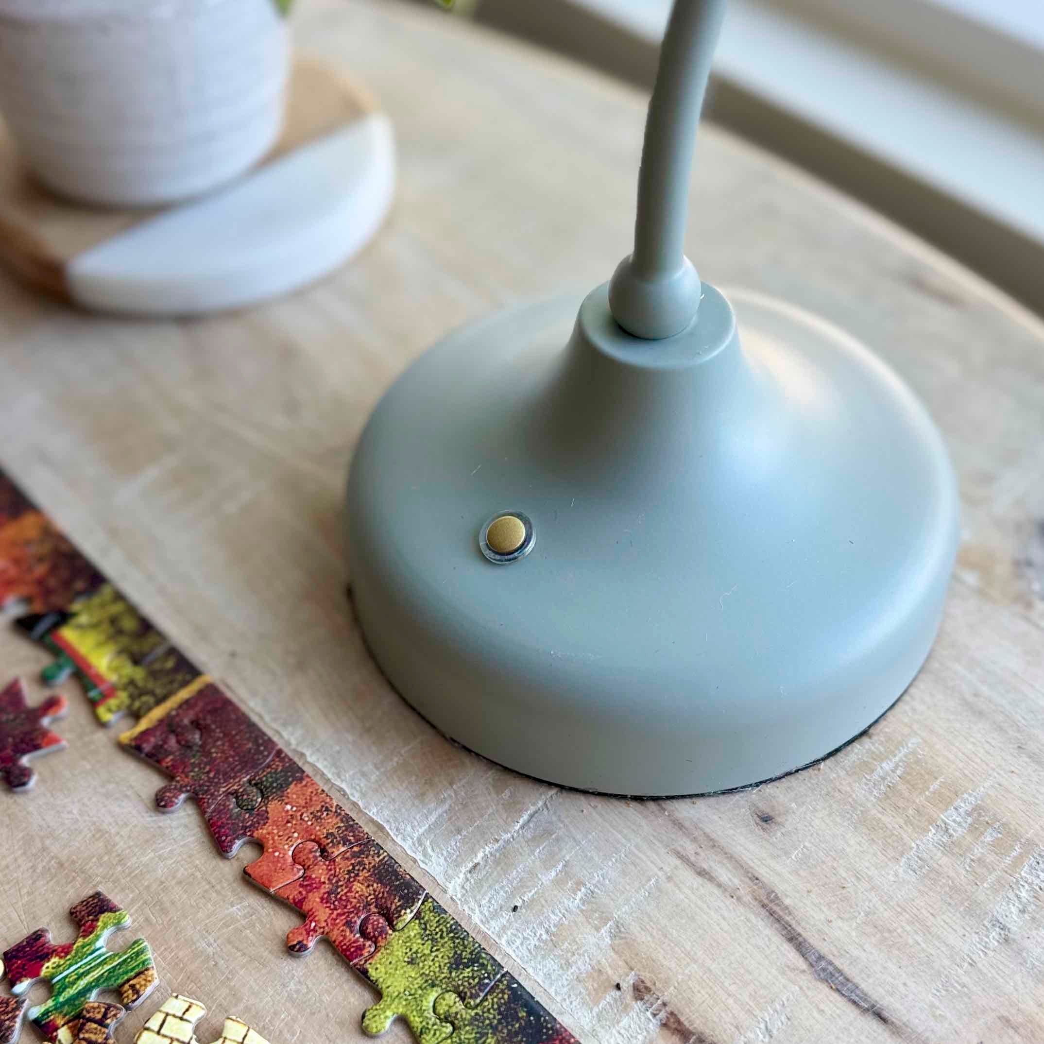 Gray lamp base on a wooden surface with a puzzle piece.