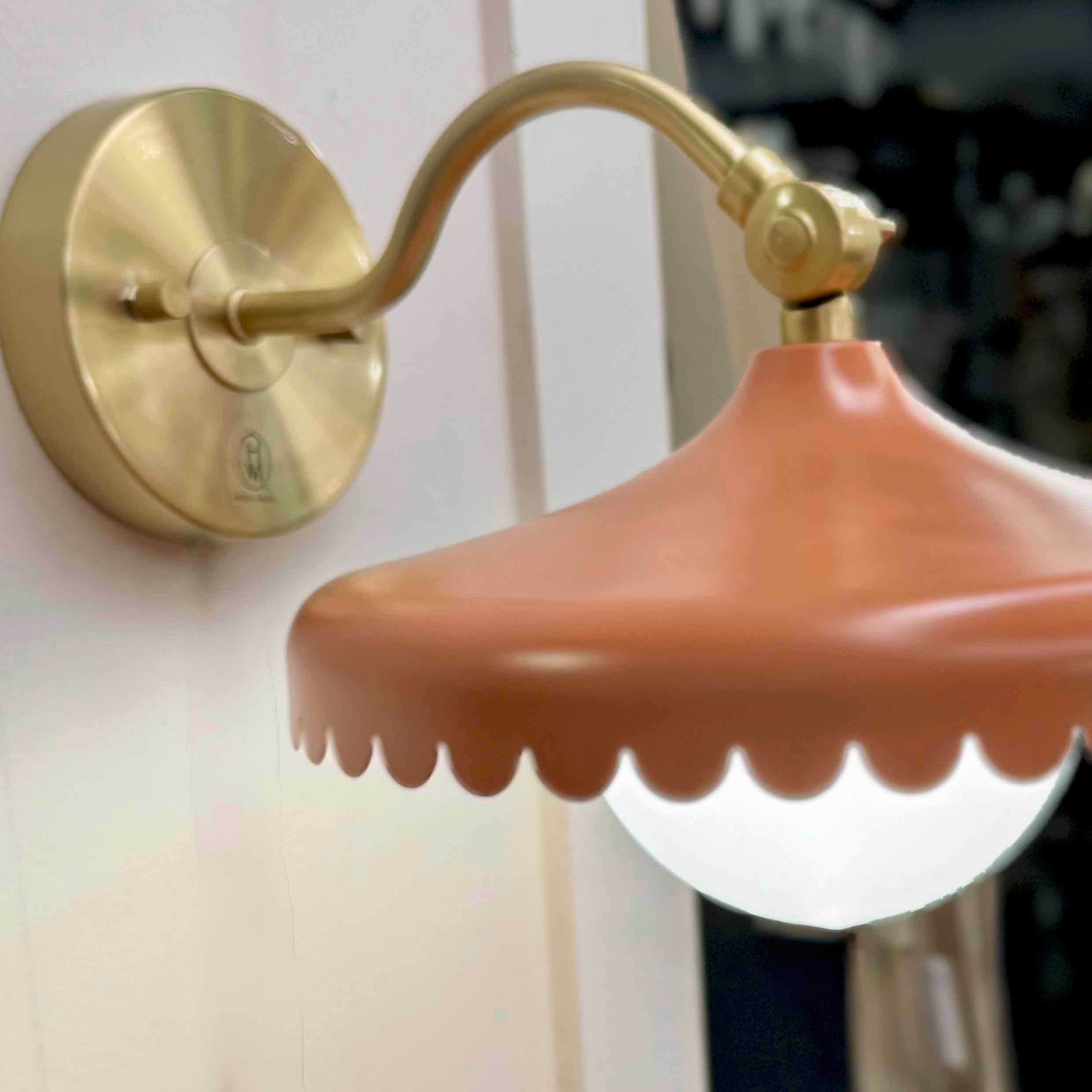 Wall-mounted lamp with a gold arm and pinkish-brown shade on a white wall.