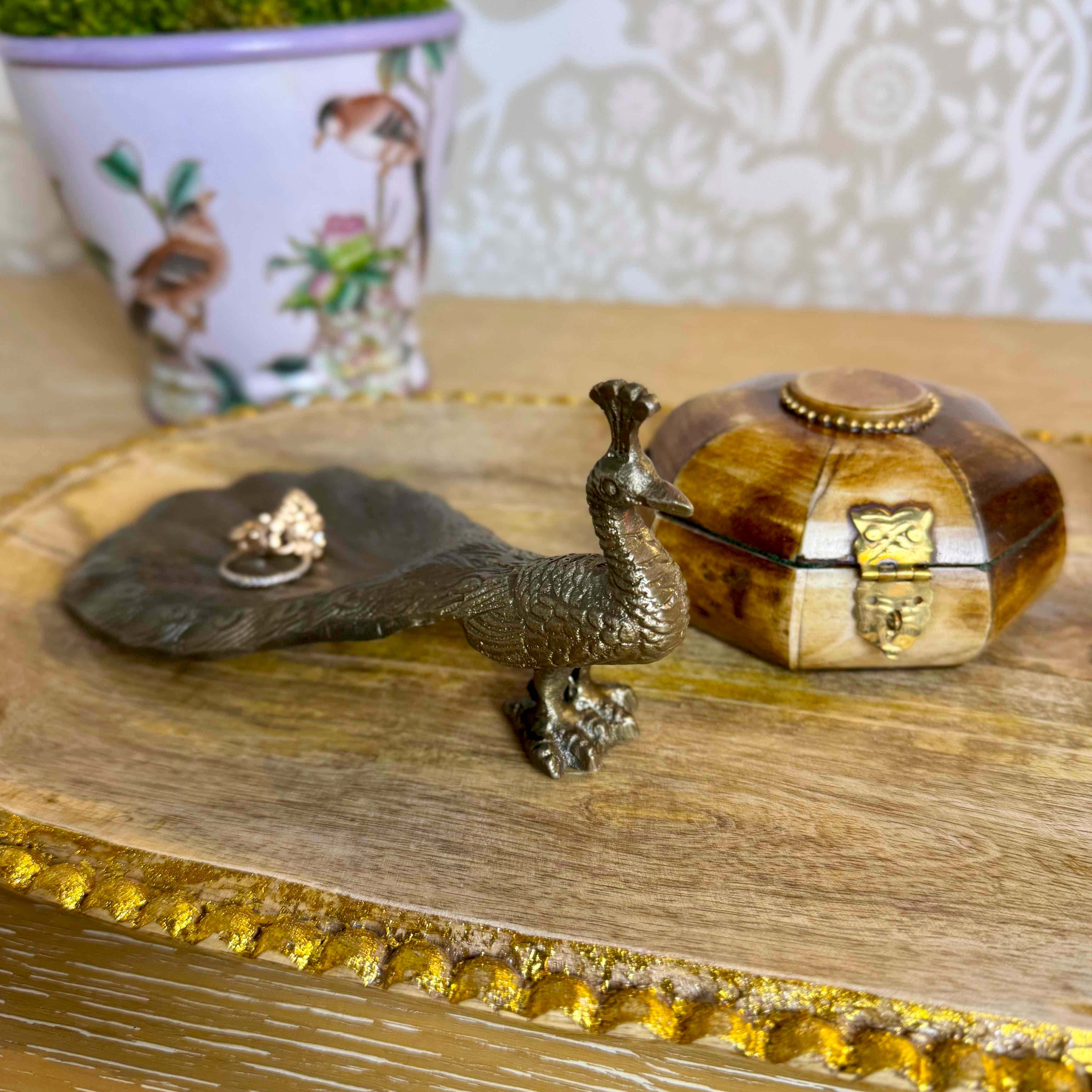 Decorative peacock figurine and wooden box on a wooden surface with a blurred background