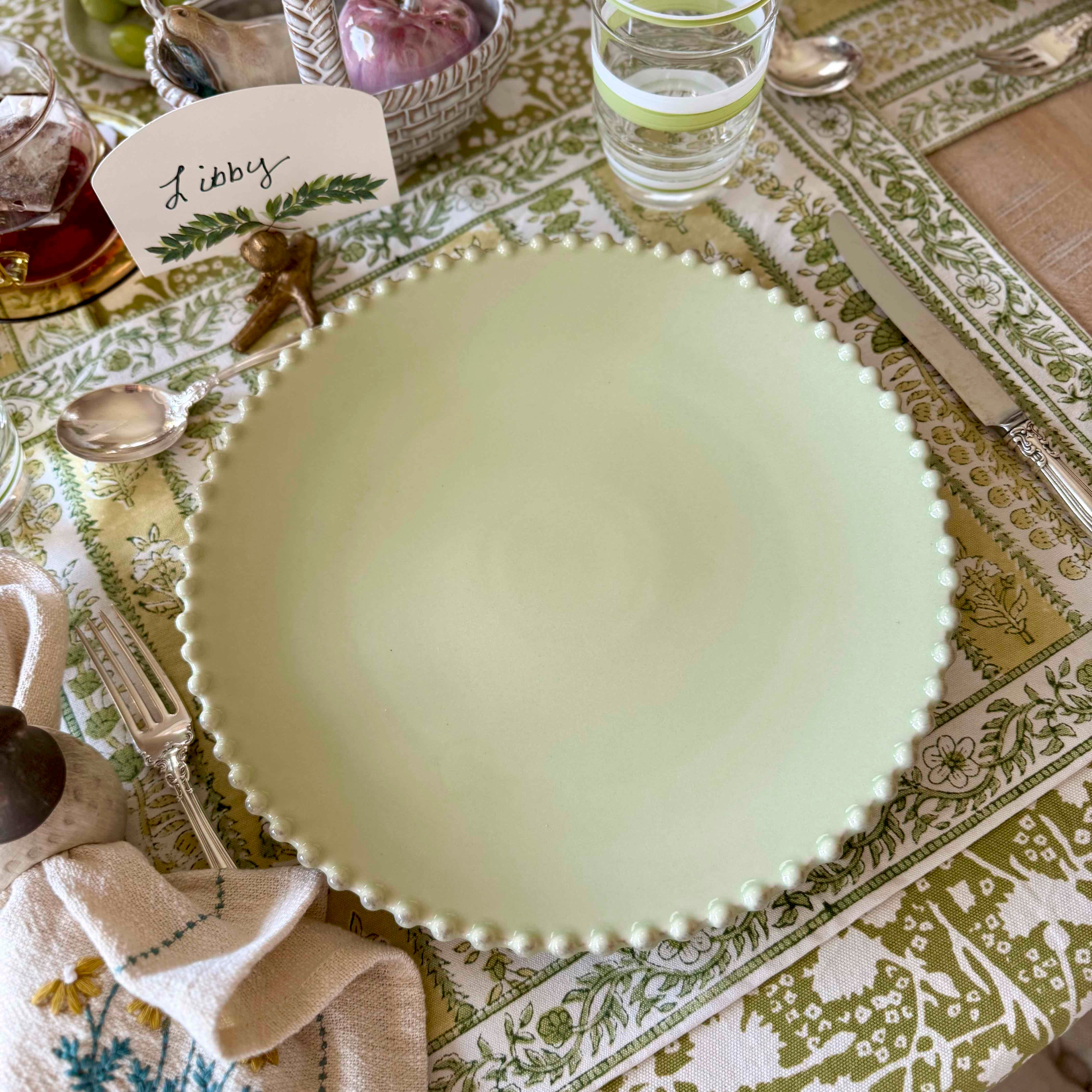 Green ceramic plate on a patterned tablecloth with a name card.