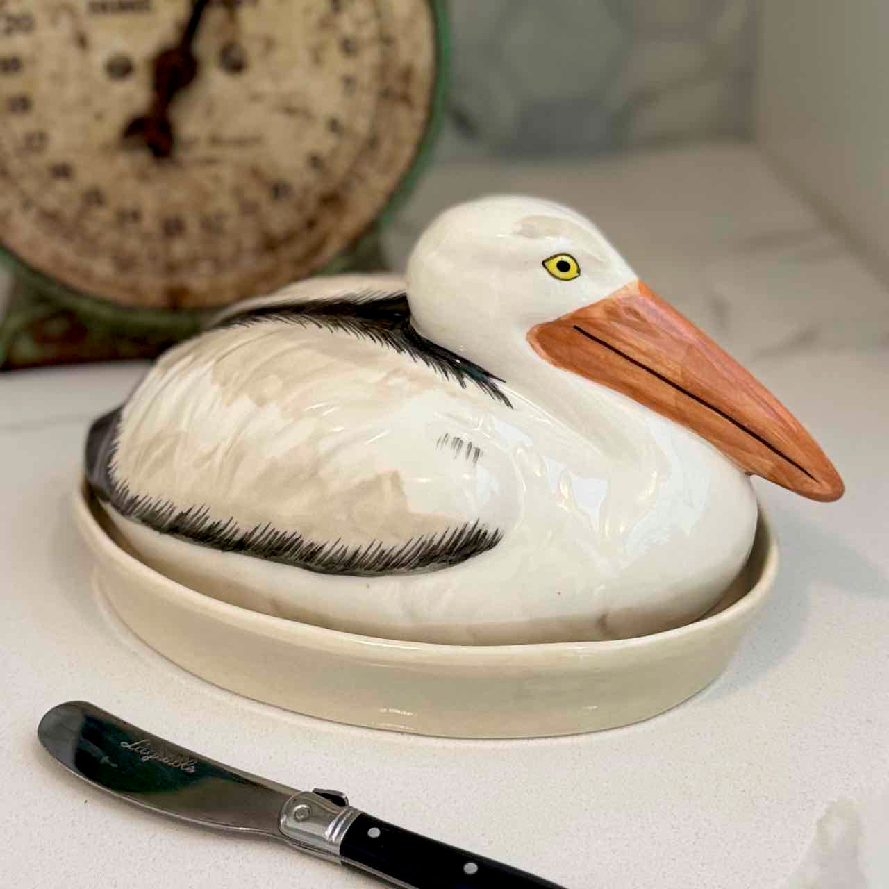 Ceramic pelican-shaped container on a white surface with a knife beside it.
