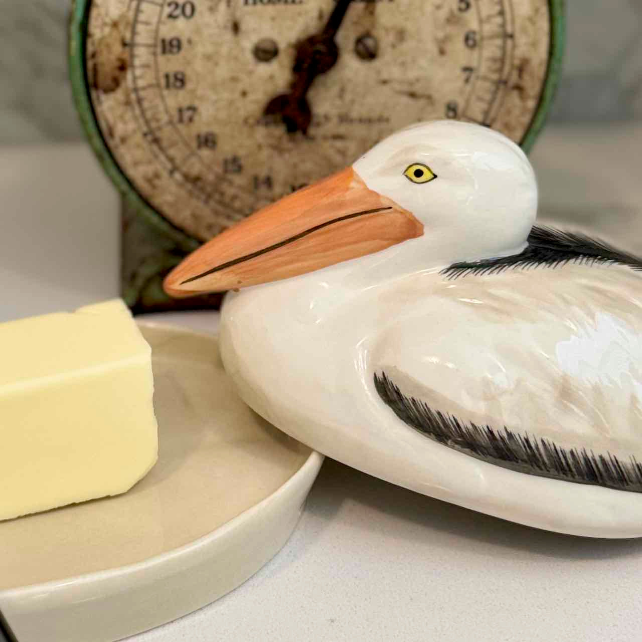 Butter dish shaped like a pelican with a clock in the background