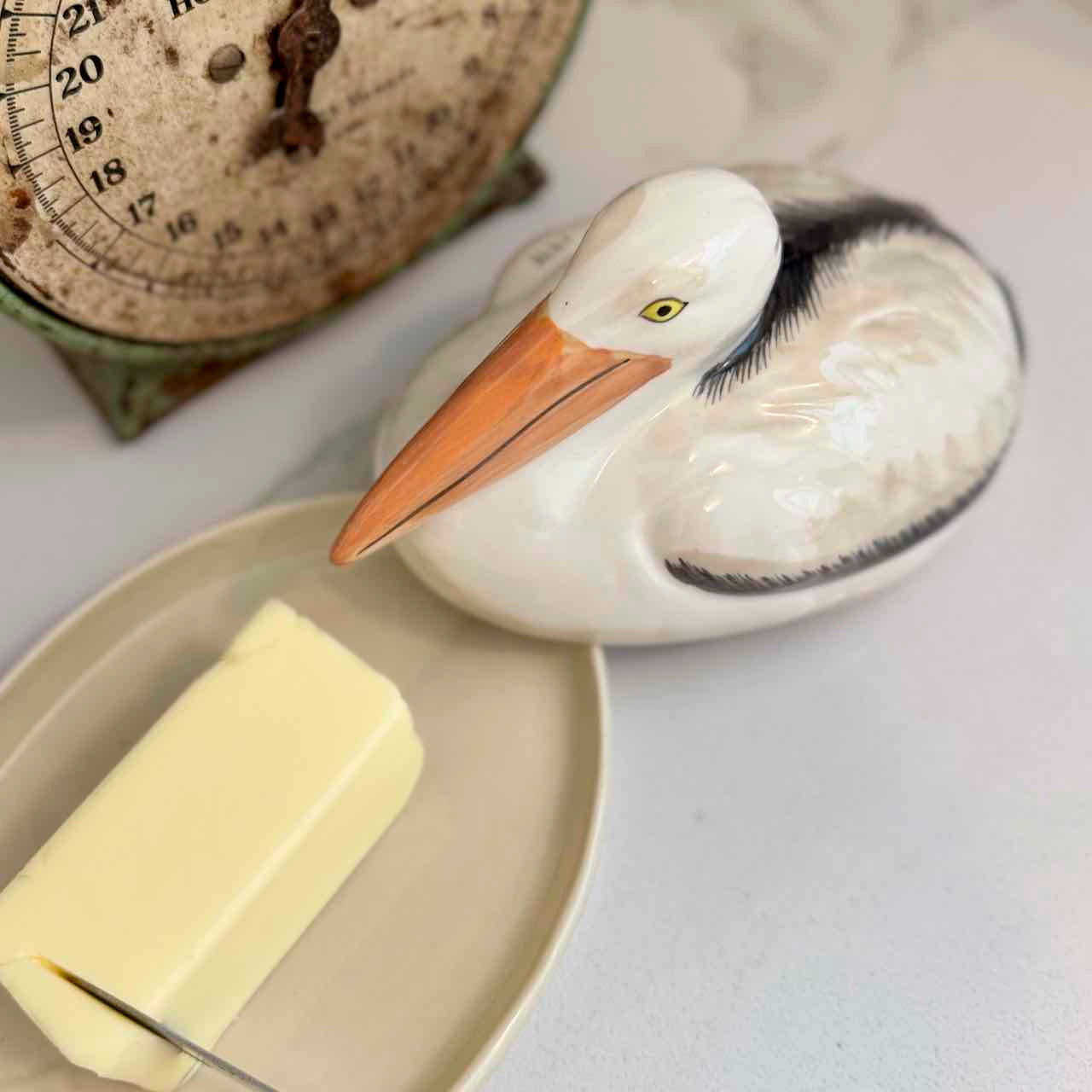 Butter dish shaped like a pelican with a stick of butter on a plate, next to an old-fashioned scale.