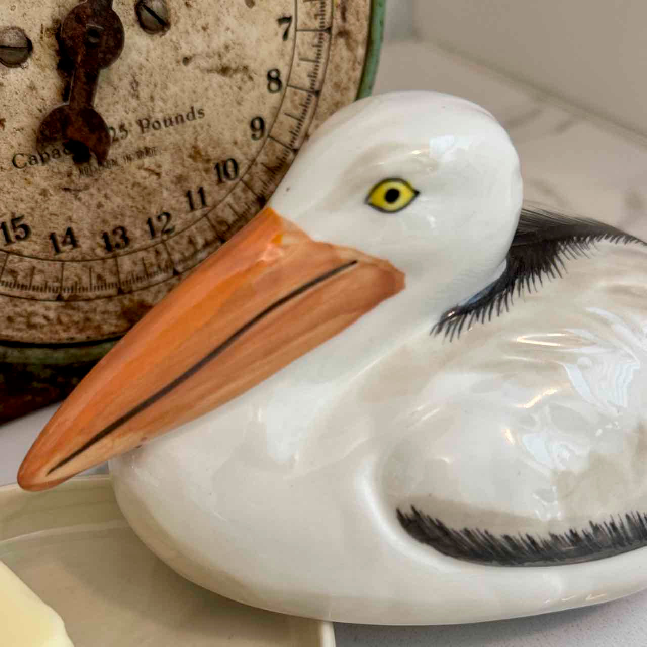 Ceramic pelican figure with an antique scale in the background