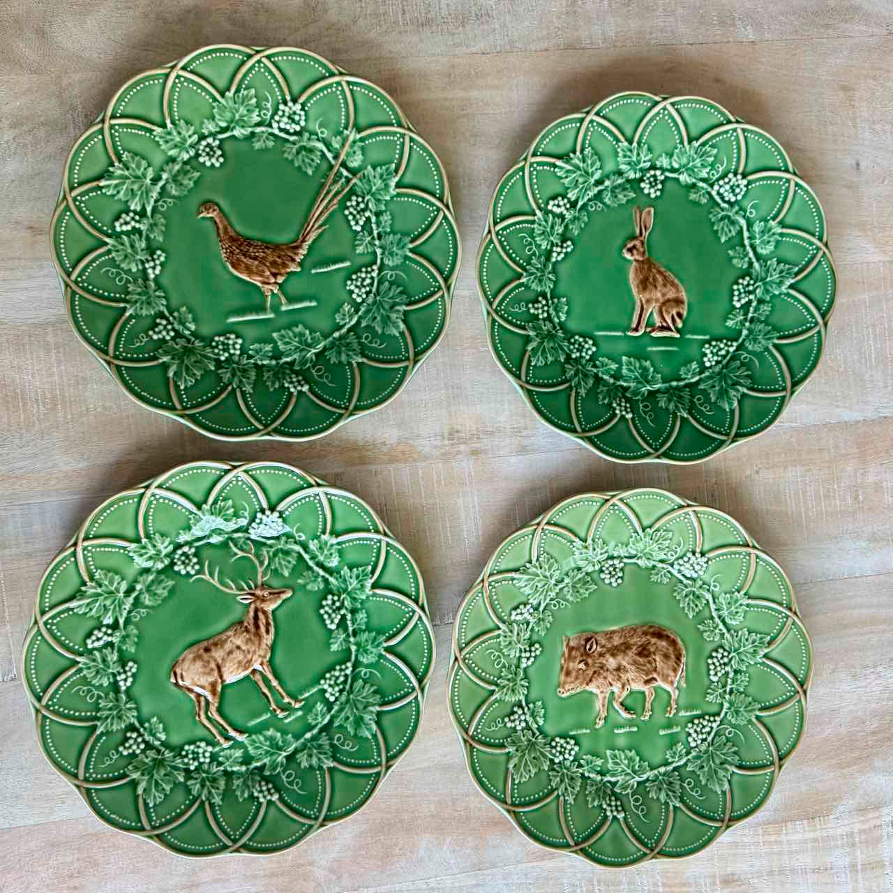 Four green ceramic plates with animal illustrations on a wooden surface