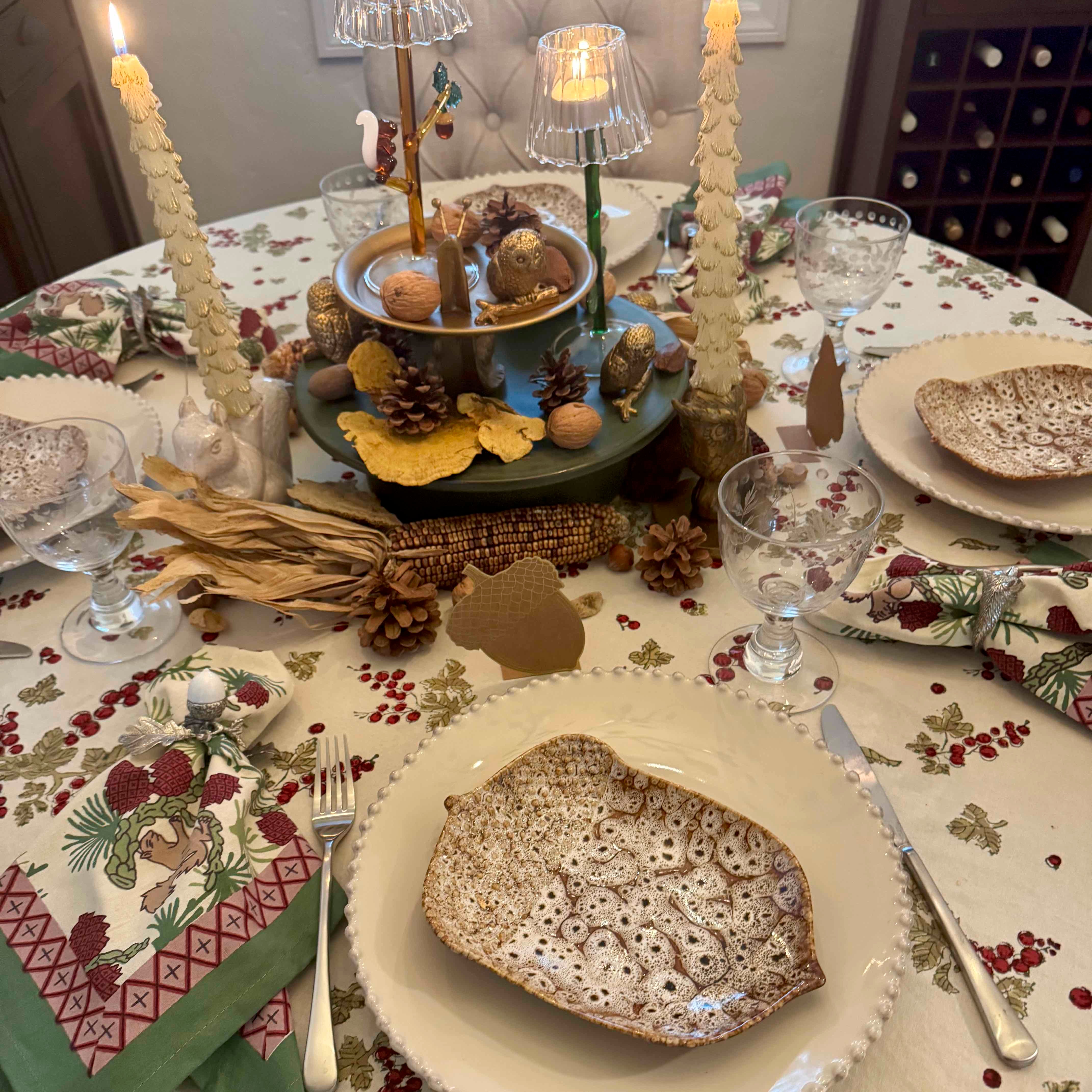 Decorative Christmas table setting with candles, plates, and glasses.