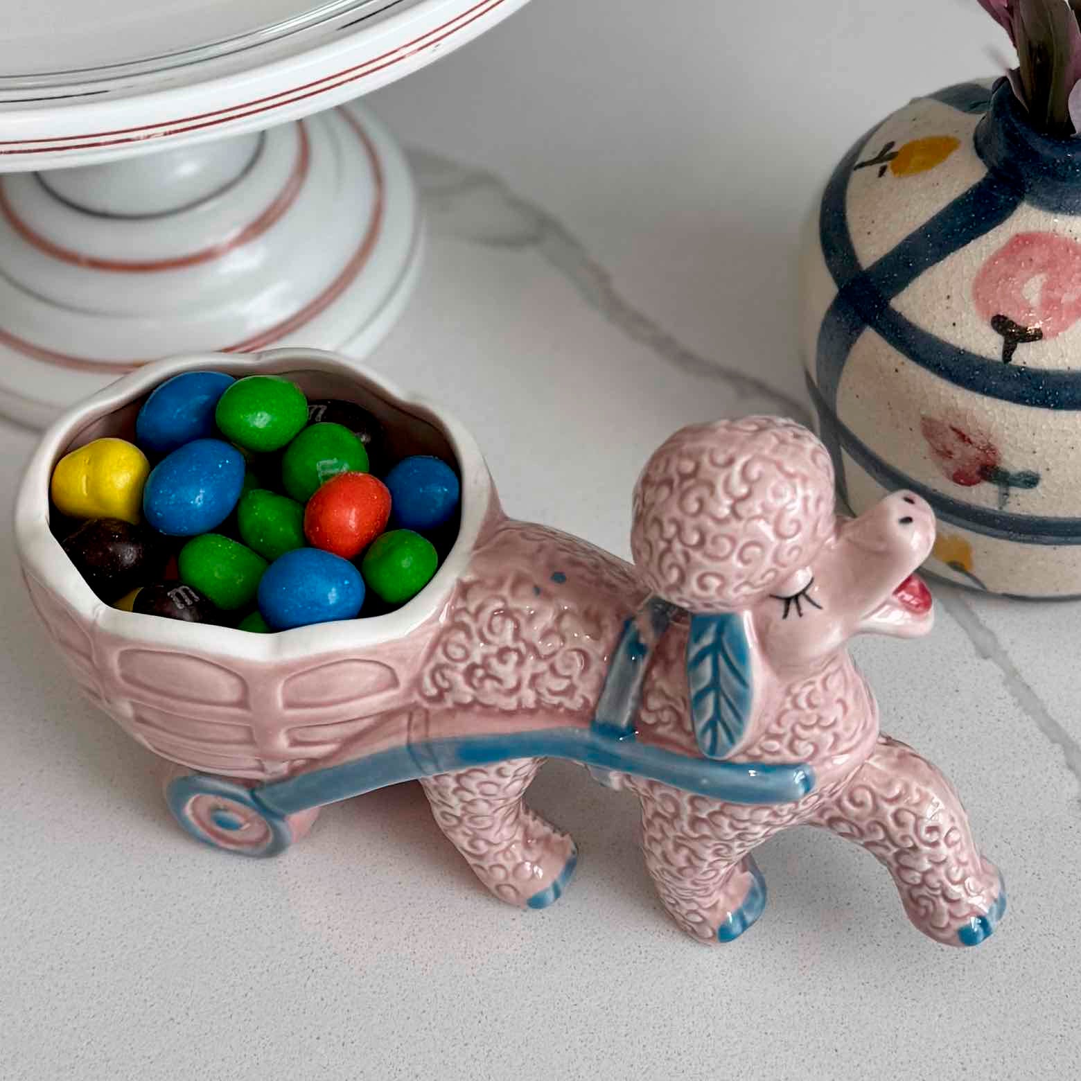 Ceramic poodle figurine with a cart full of colorful candies on a light surface.