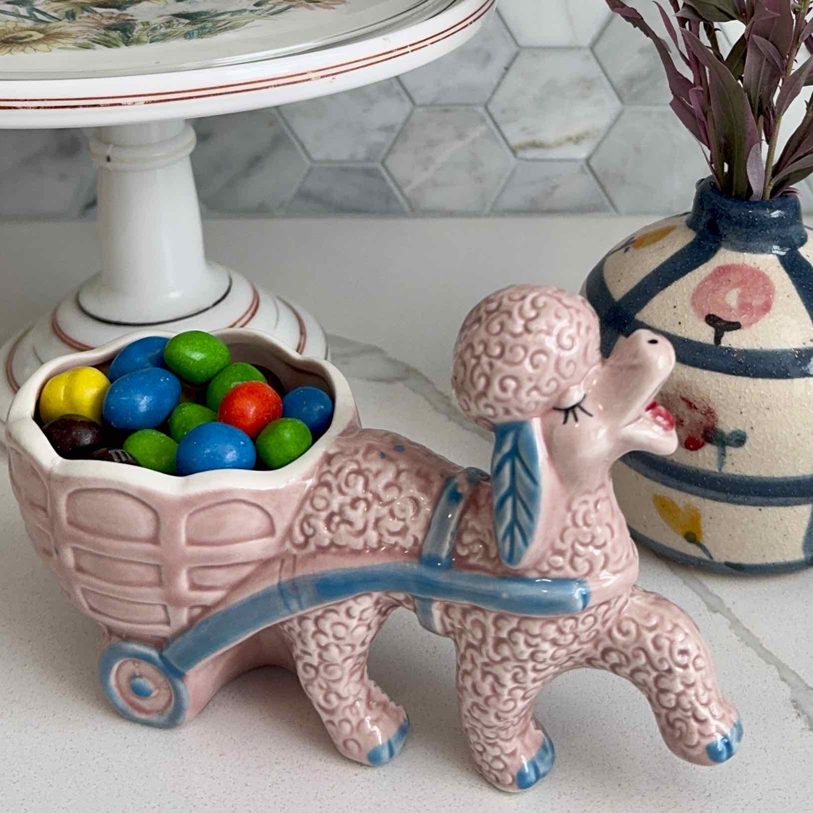 Ceramic poodle with a cart full of colorful candies on a marble surface.