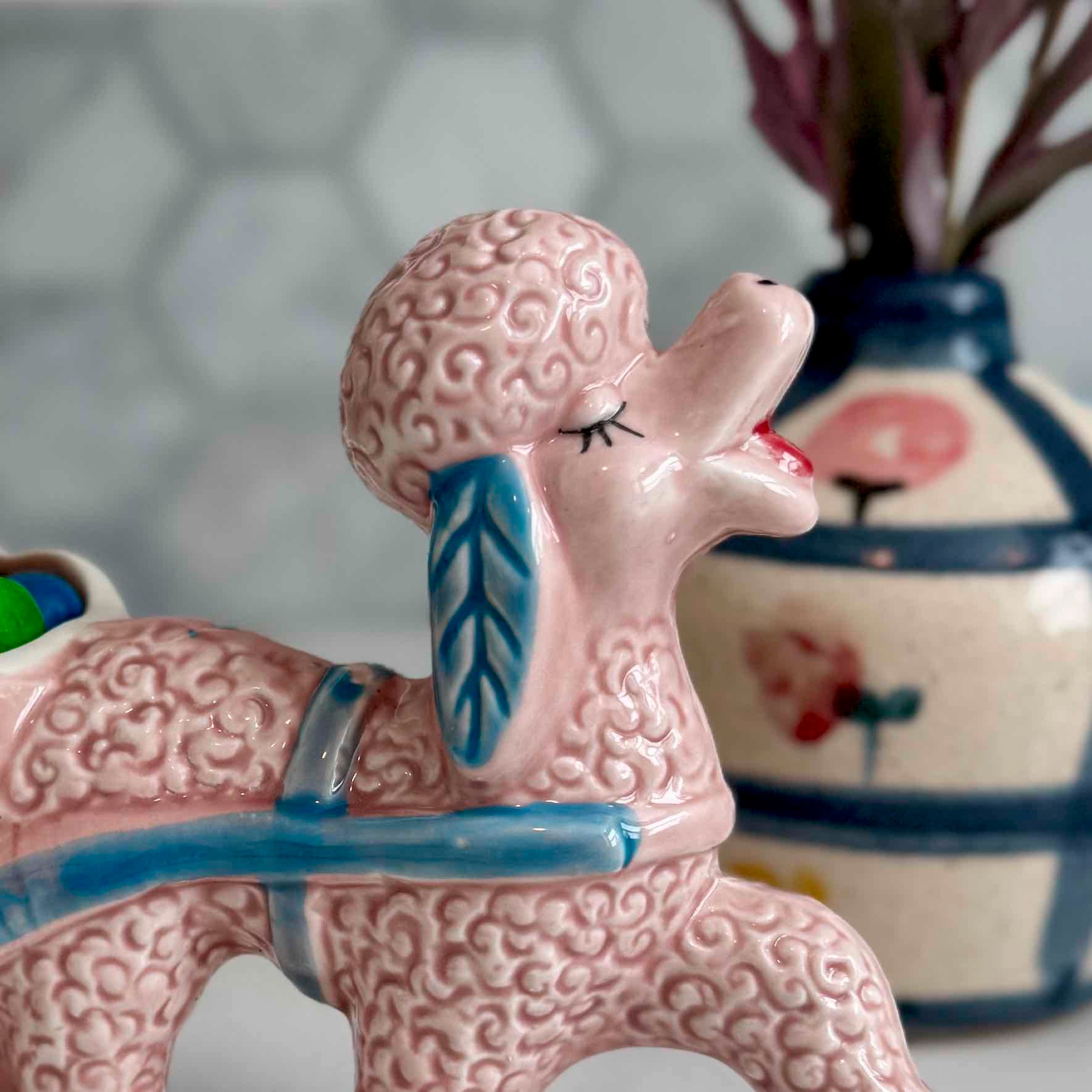 Pink ceramic poodle figurine with a brain on its head, standing in front of a decorative vase.