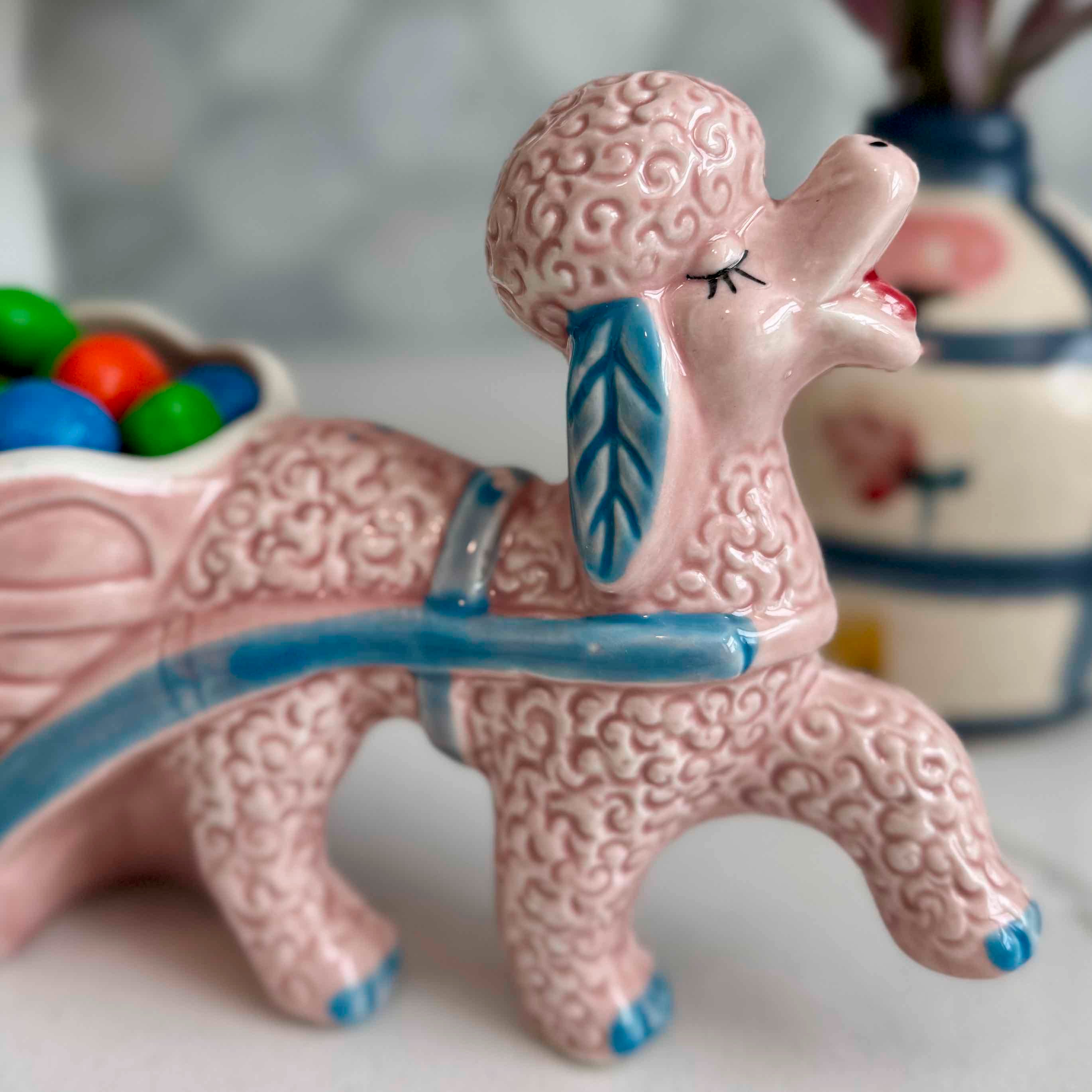 Pink ceramic poodle with a blue ribbon on a white surface